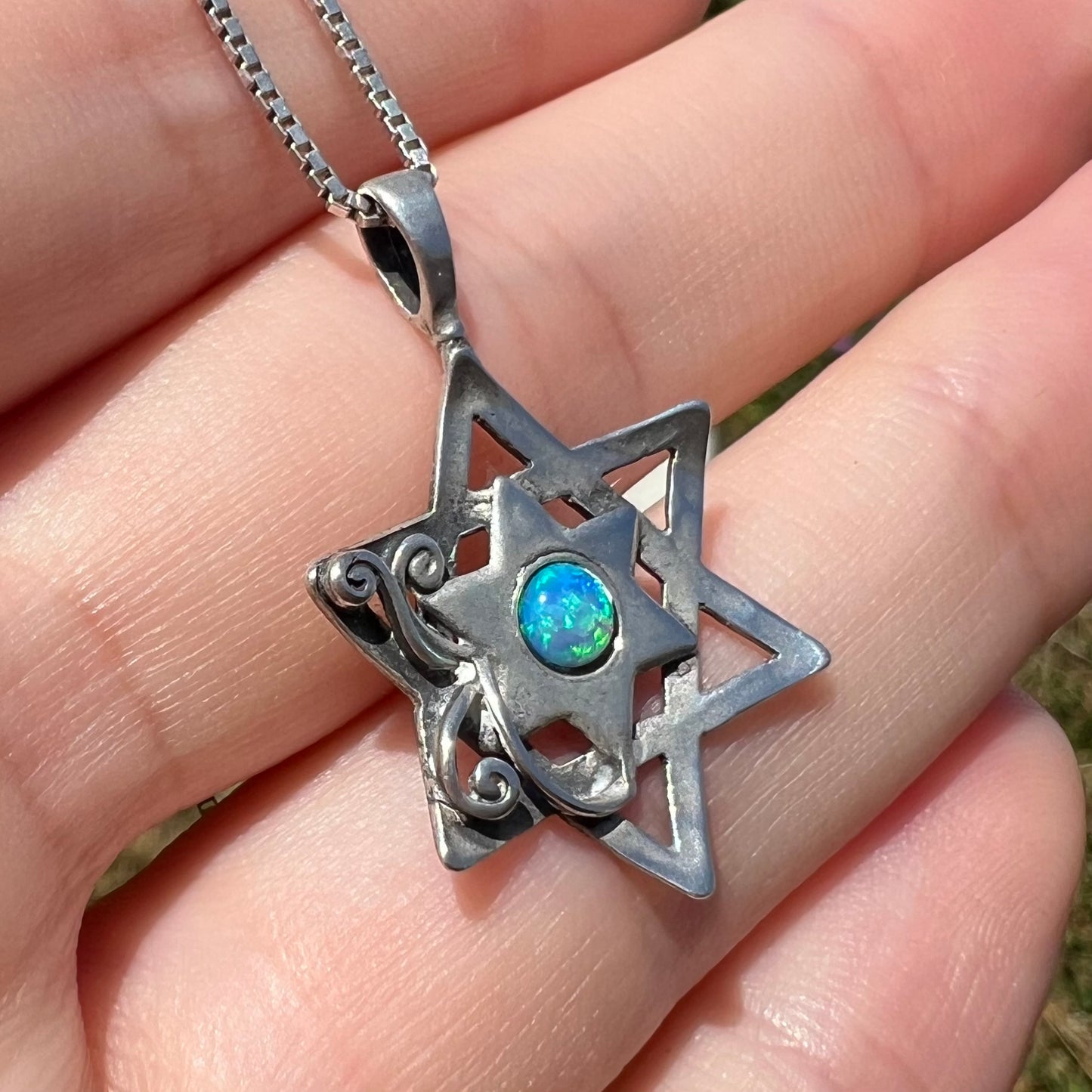 A silver Star of David necklace set with a round blue lab-created opal shown at an angle in daylight.
