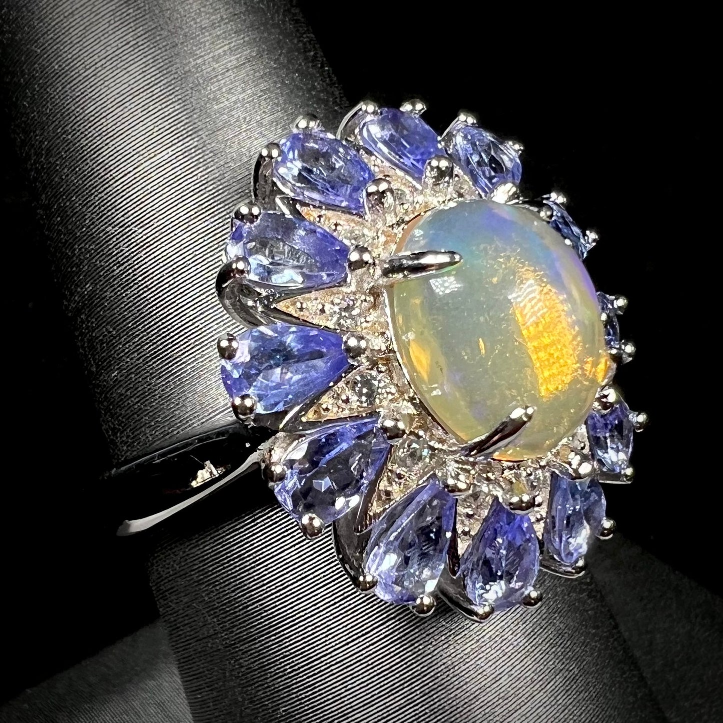 A silver opal and tanzanite halo ring shown at an angle against a black backdrop.