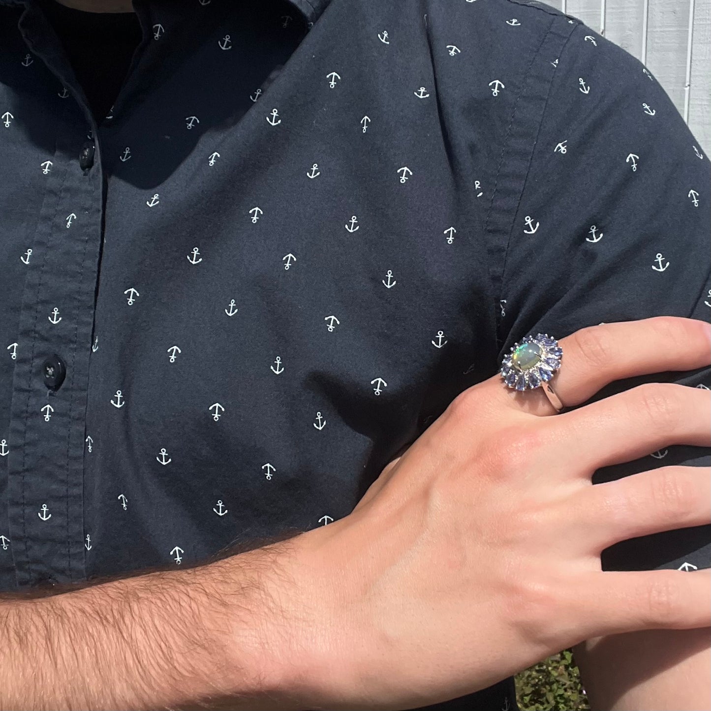 A hand resting on an opposing arm while wearing an opal and tanzanite ring in harsh natural light.