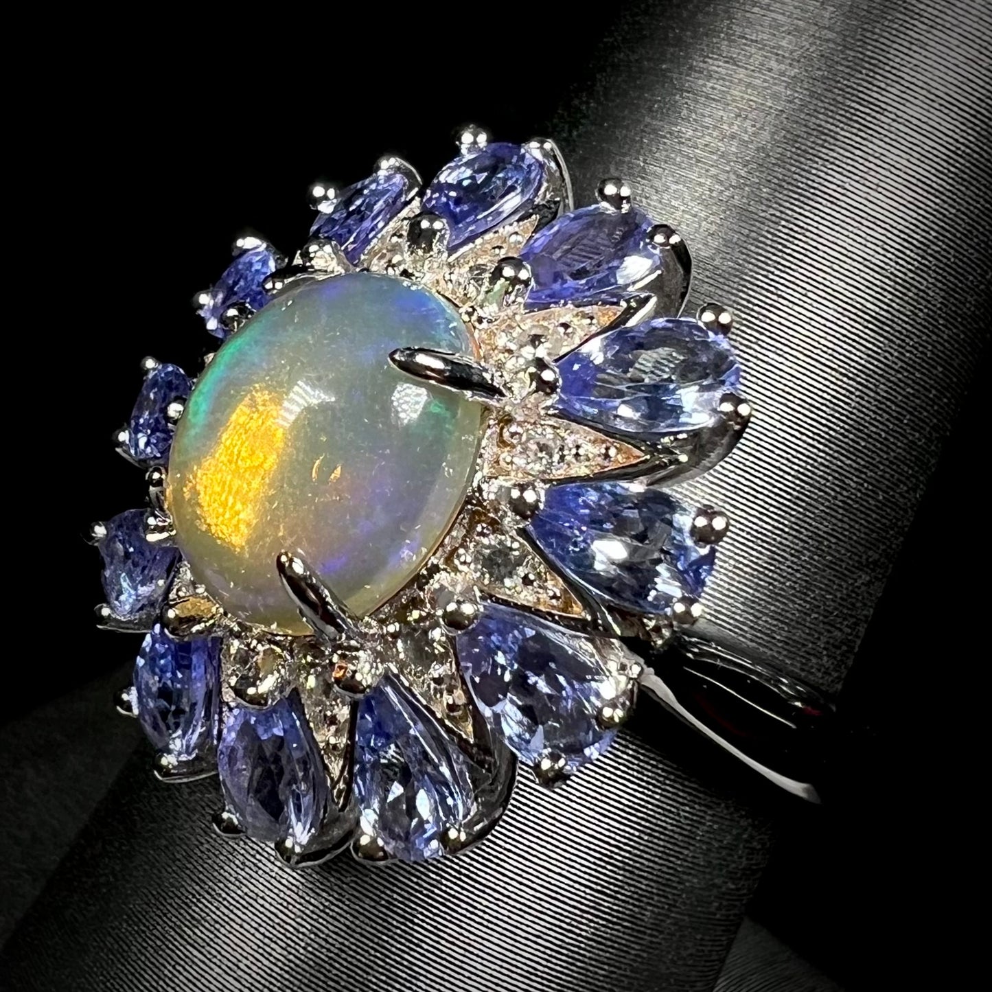 An opal tanzanite ring with white zircon accents in sterling silver, shown against dark backdrop.