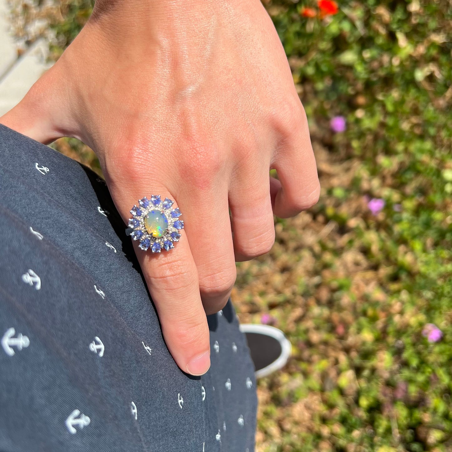 Hand resting on hip while wearing an opal and tanzanite ring on the index finger in natural sunlight.