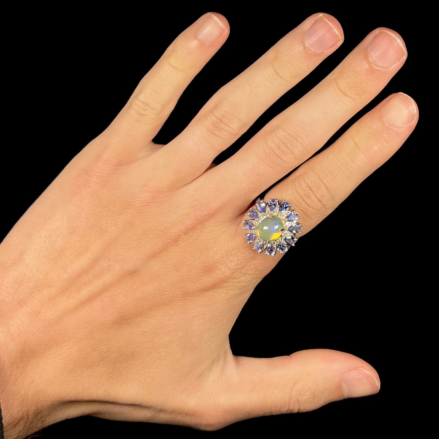 An opal and tanzanite starburst ring, worn on a hand against a black background.