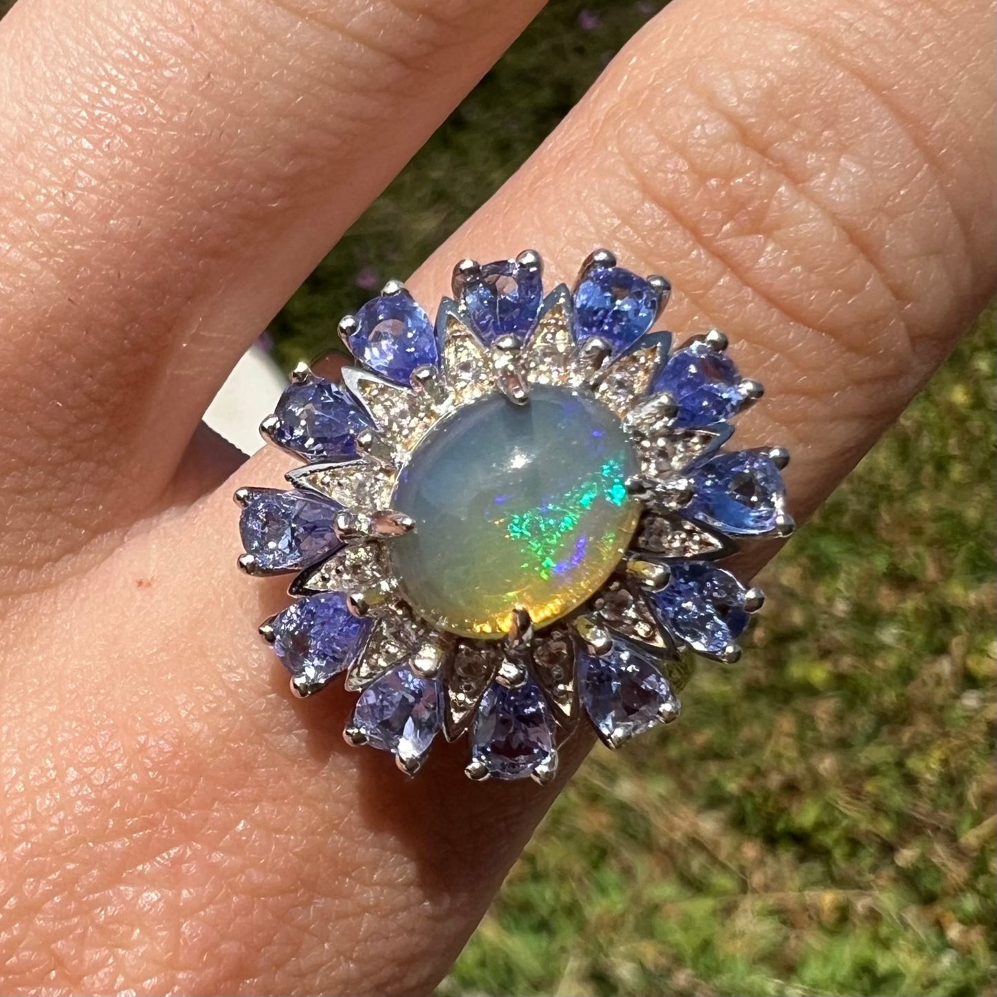 Close-up of a tanzanite starburst ring with blue color play, shown from the front worn on a finger in sunlight.