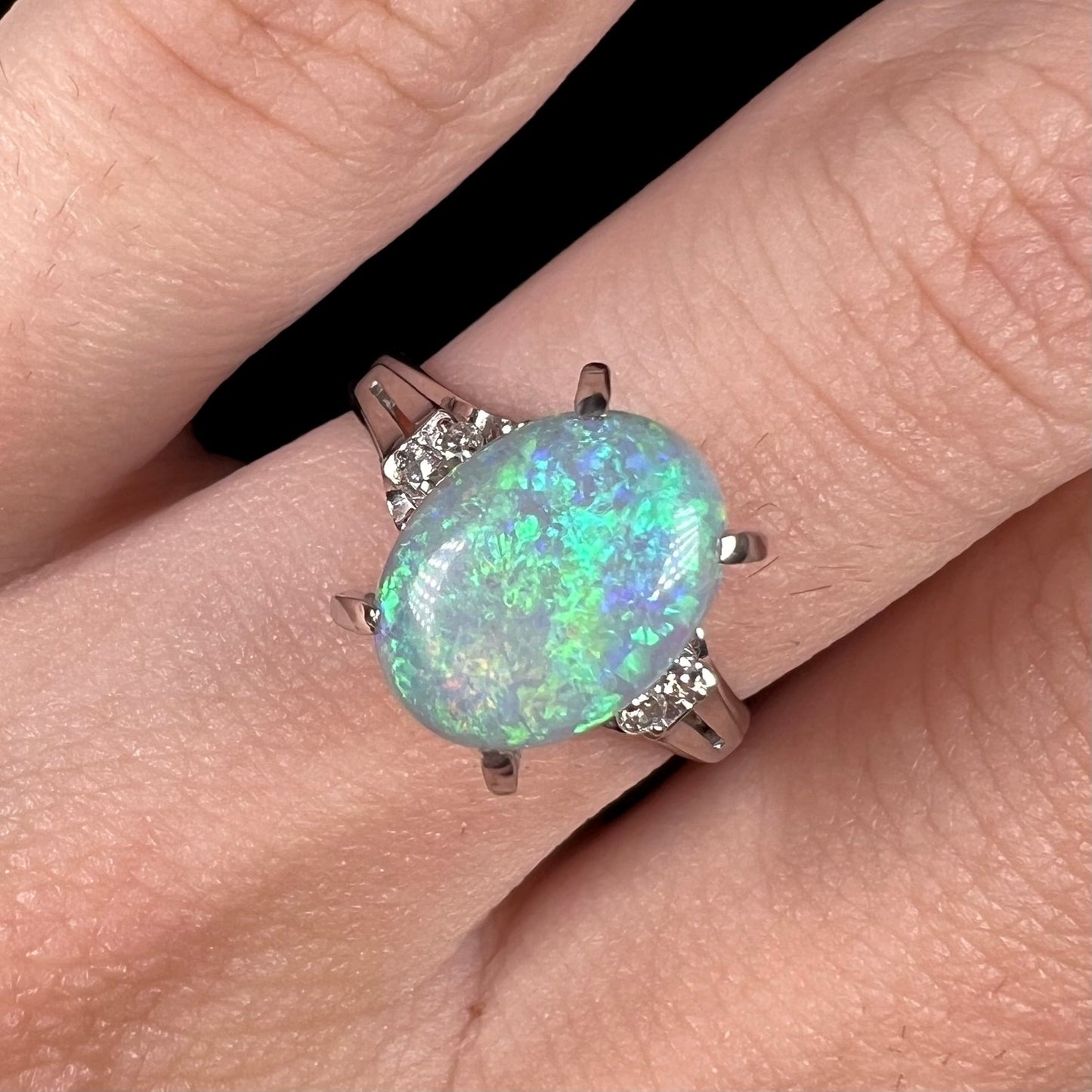 A platinum filigree opal engagement ring set with diamond accents. The opal has green-blue colors.