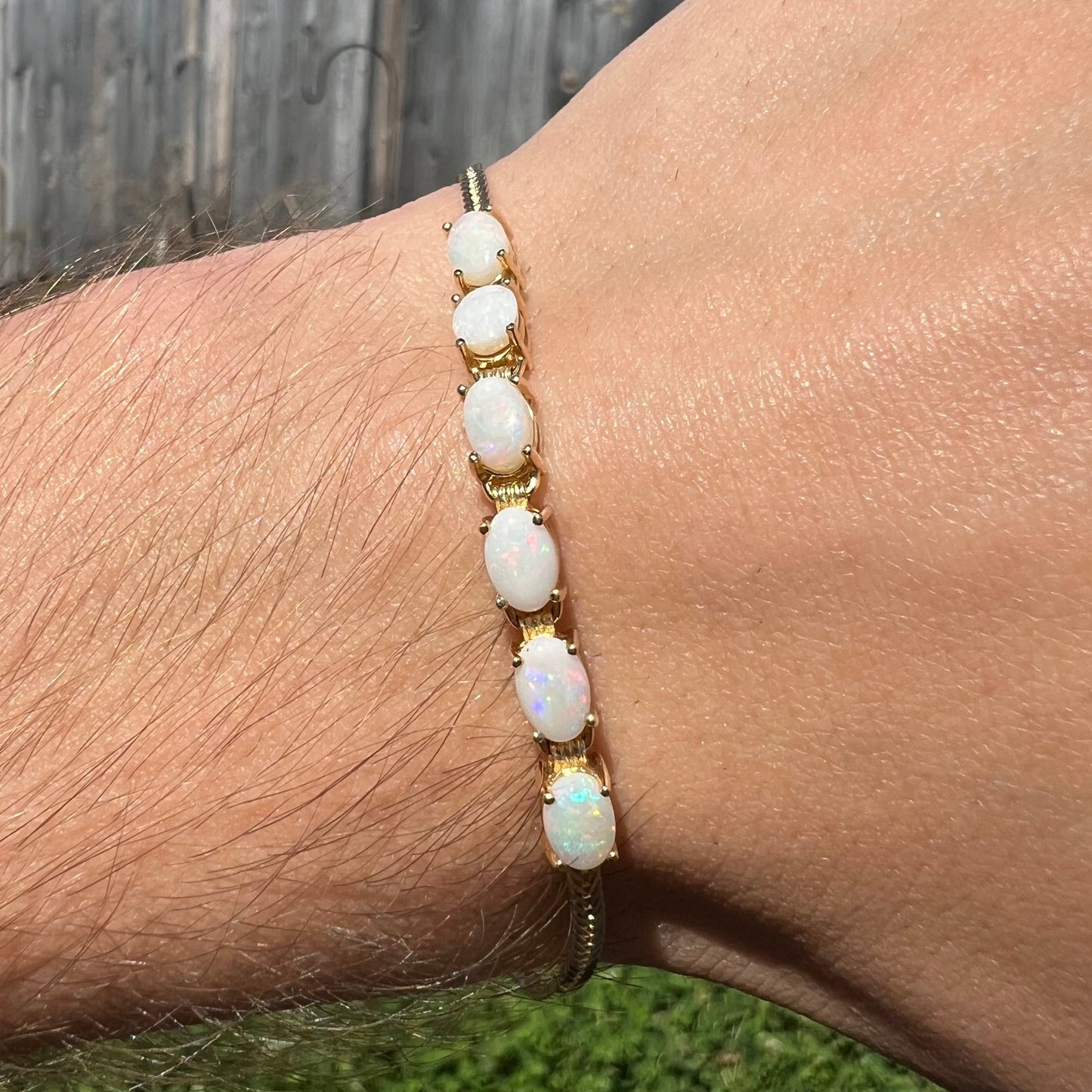 A yellow gold line bracelet set with six oval cut Australian opals.