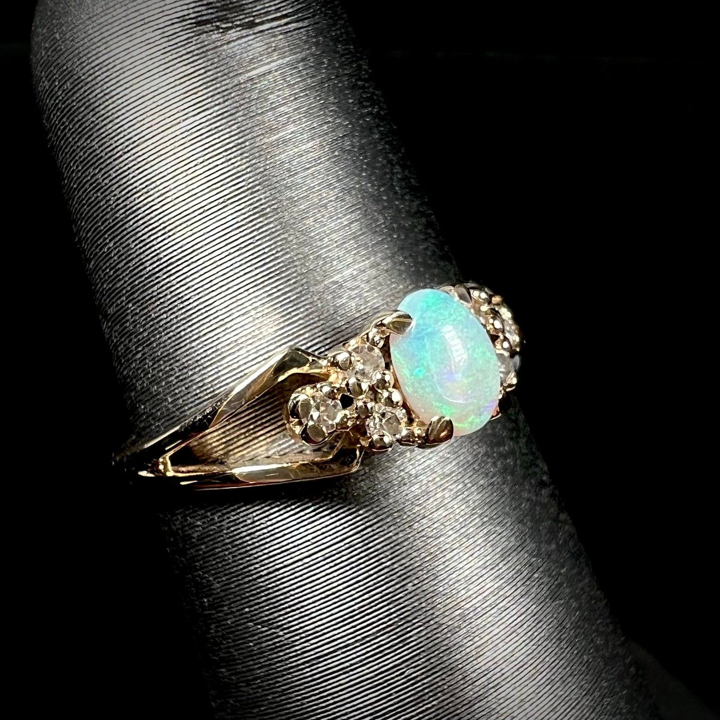 A ladies' yellow gold opal and diamond pinkie ring. The ring is a small size, and the opal shines green and blue colors.