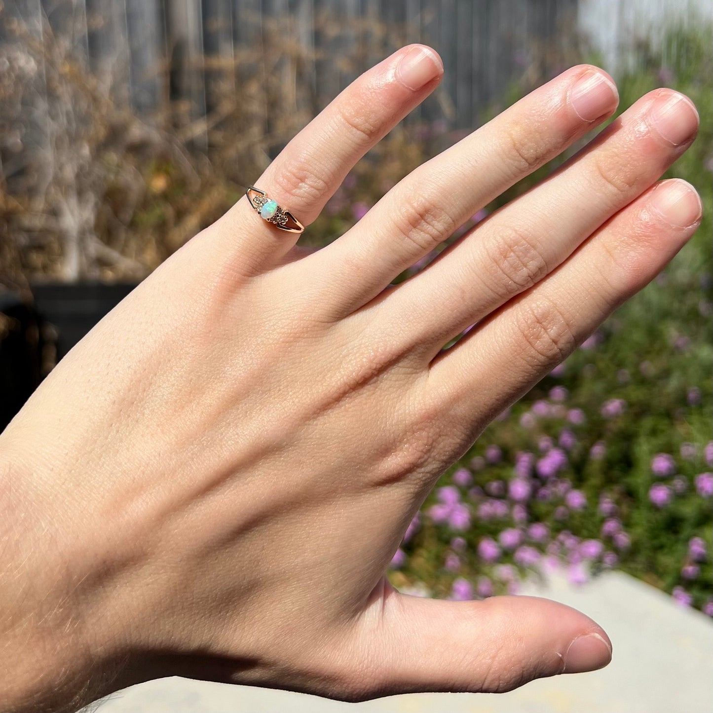 A ladies' yellow gold opal and diamond pinkie ring. The ring is a small size, and the opal shines green and blue colors.