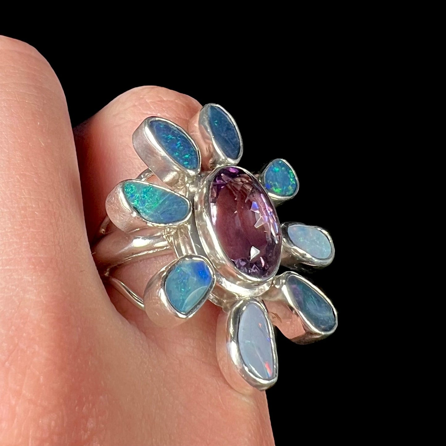 A sterling silver flower shaped ring set with an oval cut amethyst in the center and black opal doublet petals.