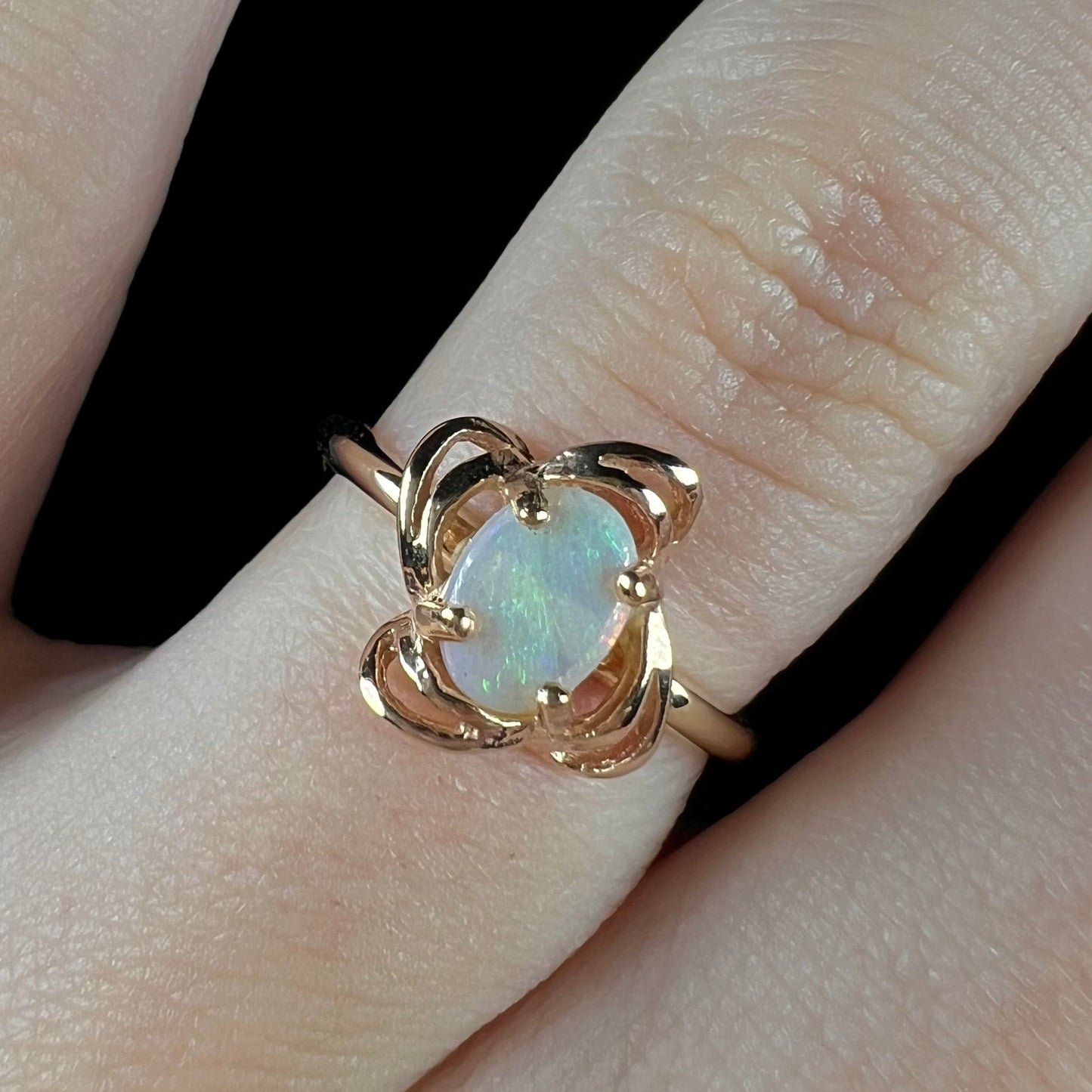 A yellow gold ring mounted with an oval cut opal. The opal has a white base tone with green and blue color play.