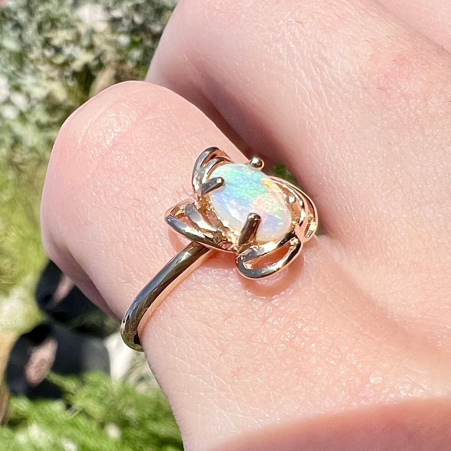 A yellow gold ring mounted with an oval cut opal. The opal has a white base tone with green and blue color play.