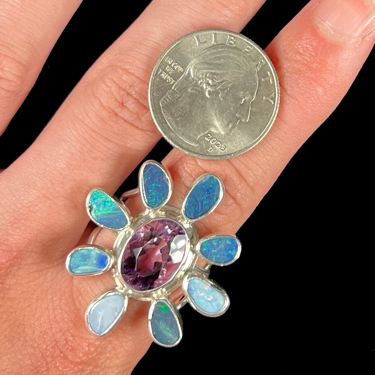 A sterling silver flower shaped ring set with an oval cut amethyst in the center and black opal doublet petals.