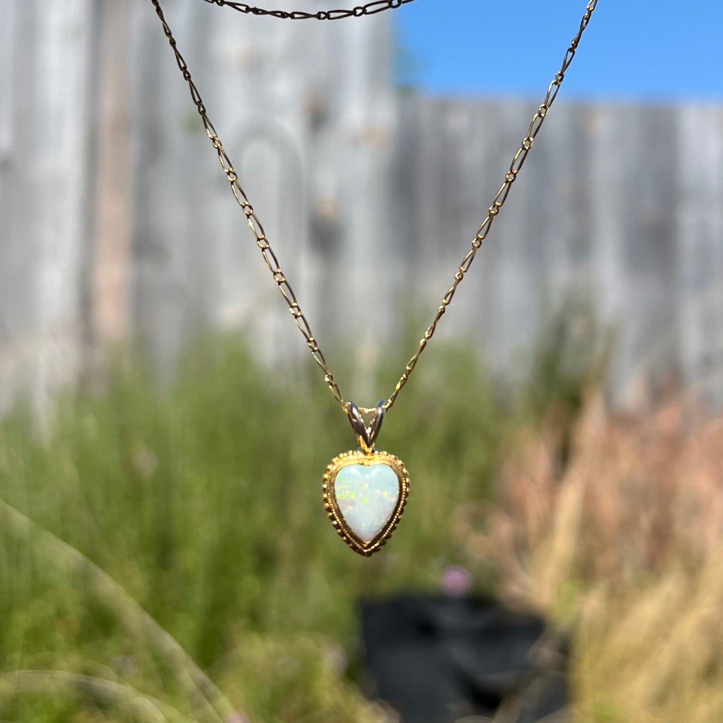 A yellow gold heart necklace mounted with a heart shaped white opal.