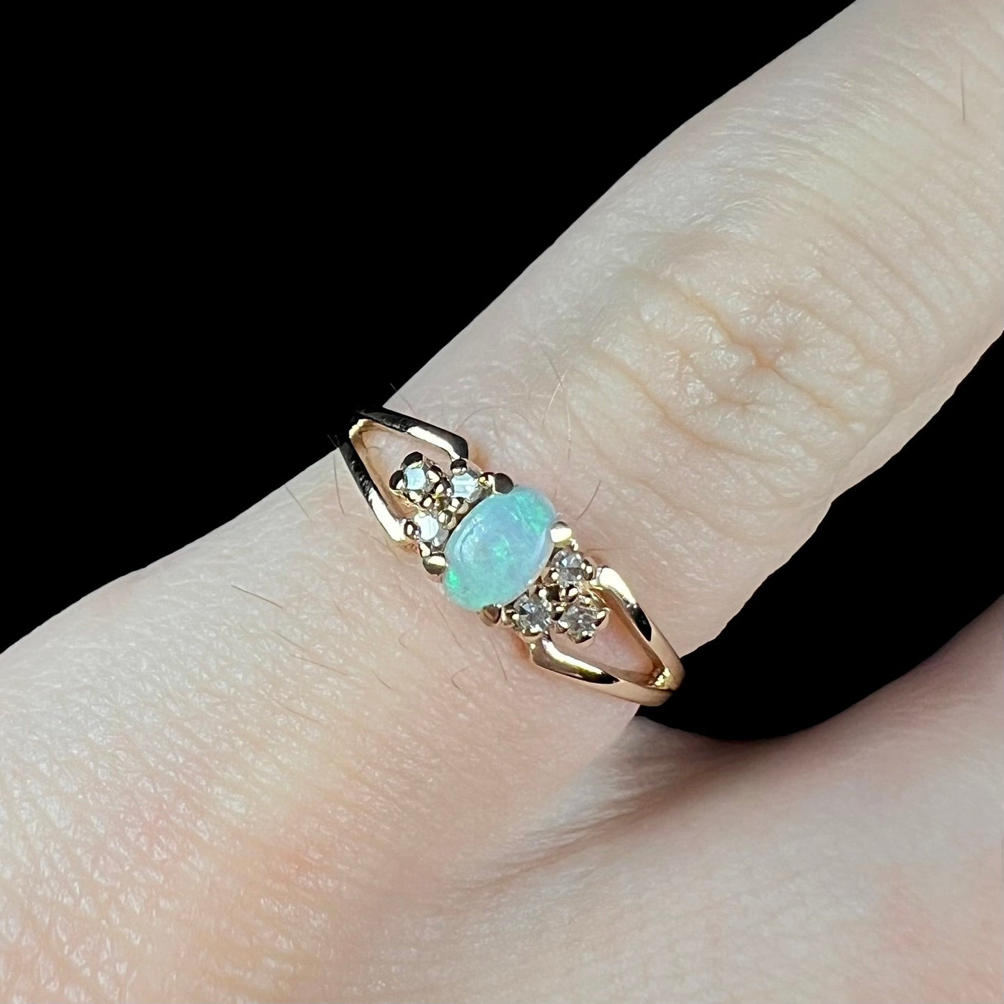A ladies' yellow gold opal and diamond pinkie ring. The ring is a small size, and the opal shines green and blue colors.