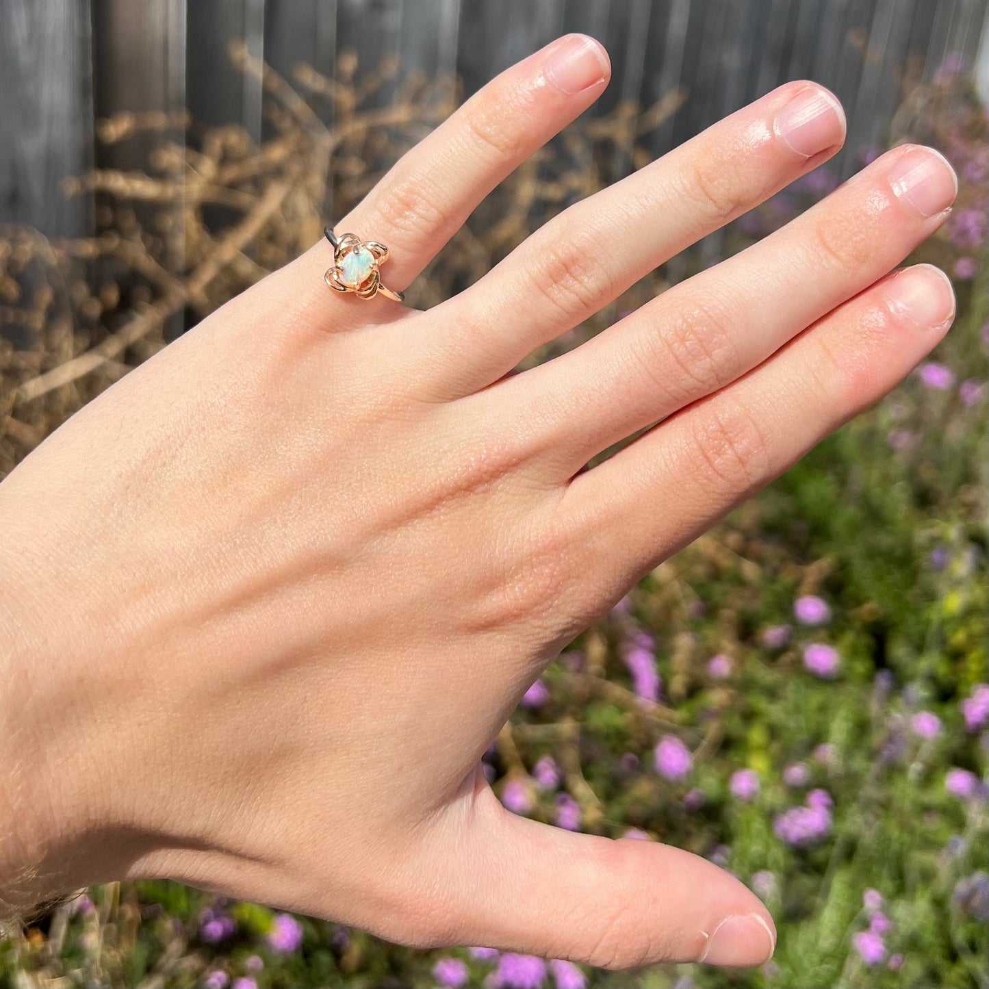 A yellow gold ring mounted with an oval cut opal. The opal has a white base tone with green and blue color play.