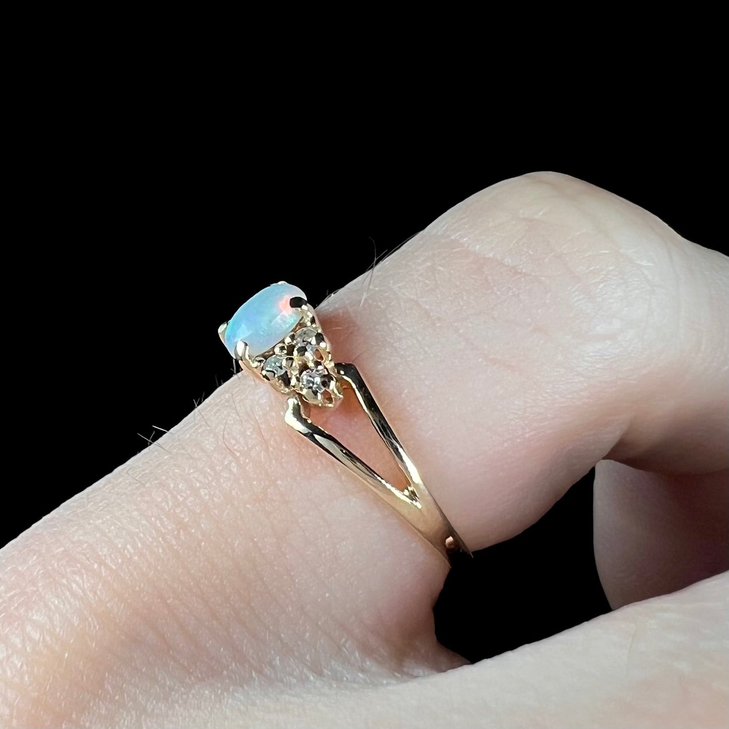 A ladies' yellow gold opal and diamond pinkie ring. The ring is a small size, and the opal shines green and blue colors.