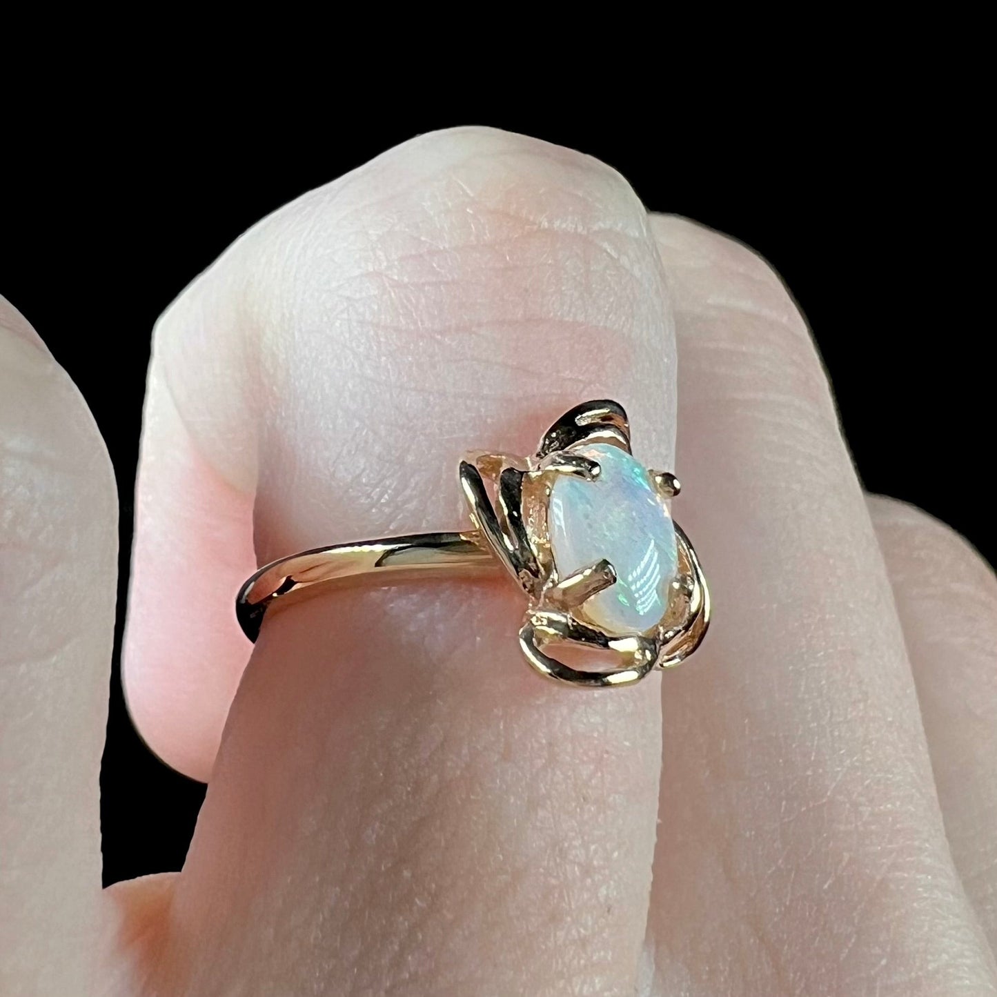 A yellow gold ring mounted with an oval cut opal. The opal has a white base tone with green and blue color play.
