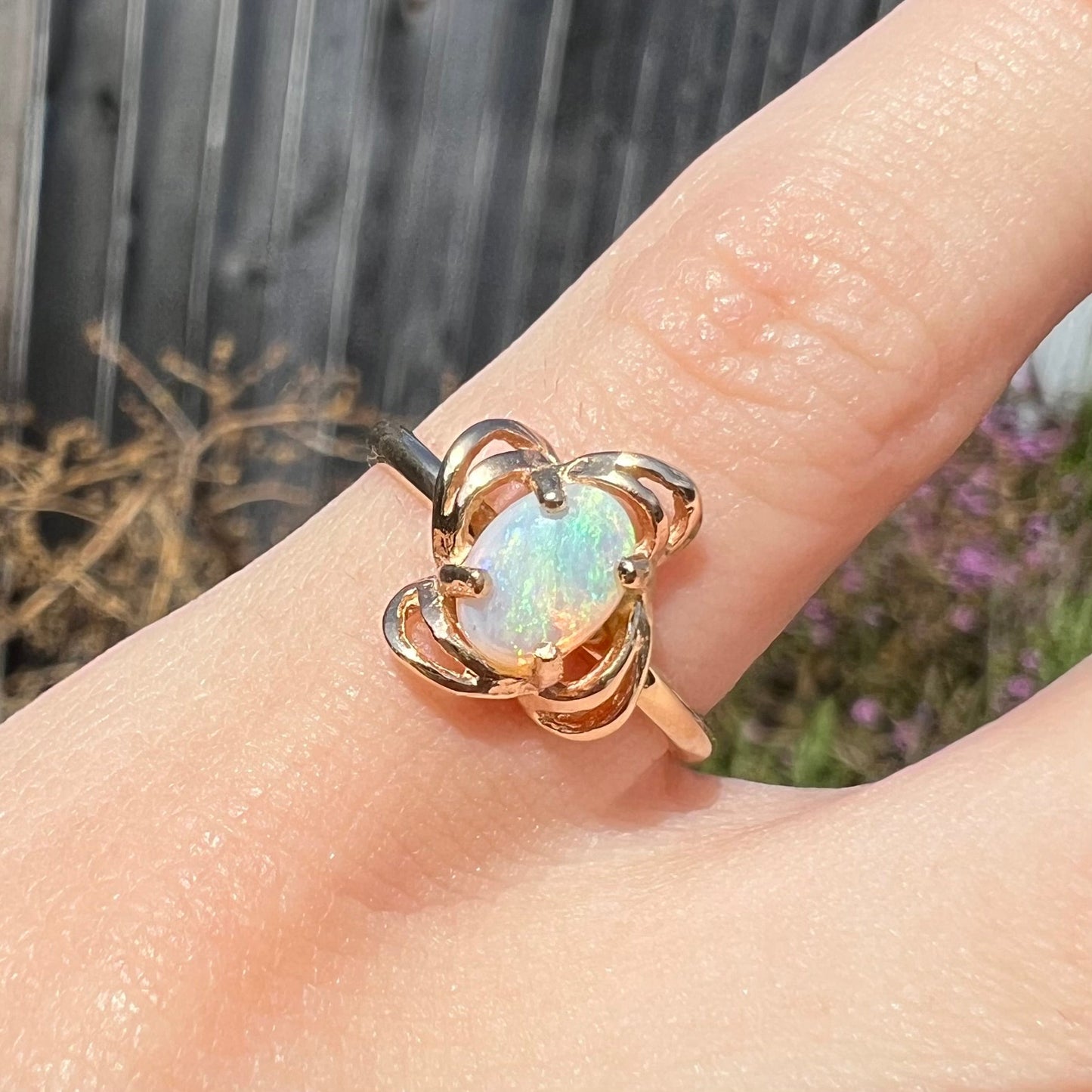 A yellow gold ring mounted with an oval cut opal. The opal has a white base tone with green and blue color play.