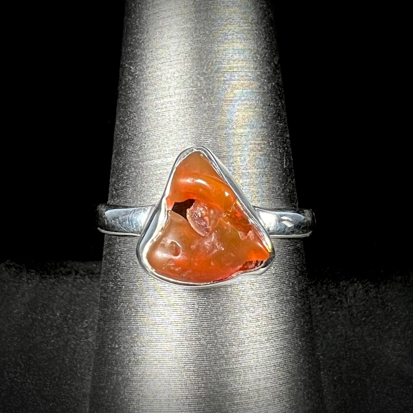 A polished fire opal crystal bezel set into a sterling silver ring. The opal is an orange color.
