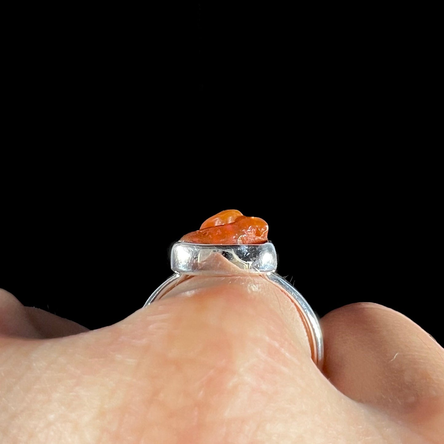 A polished fire opal crystal bezel set into a sterling silver ring. The opal is an orange color.