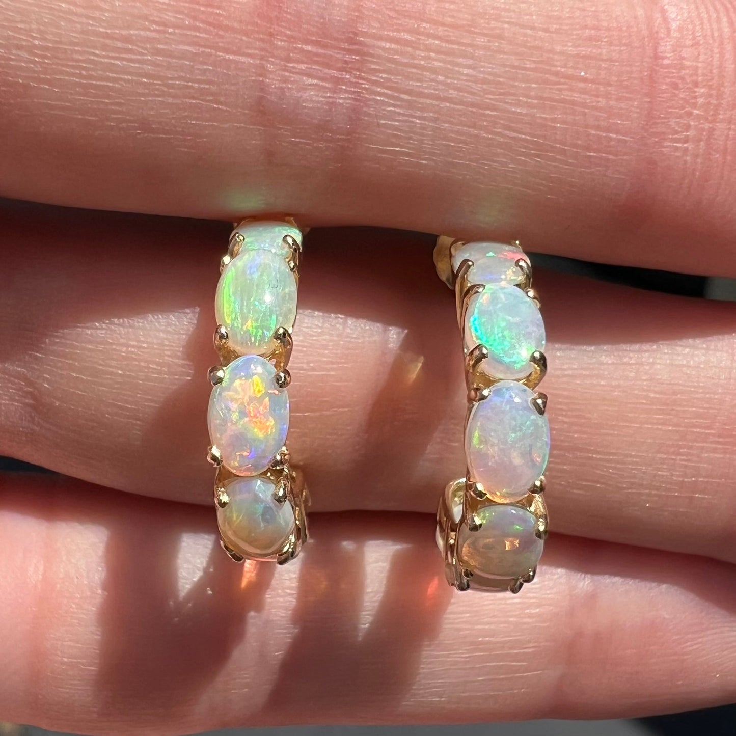 A pair of yellow gold opal hoop earrings. Each earring is set with six natural oval cut opals.
