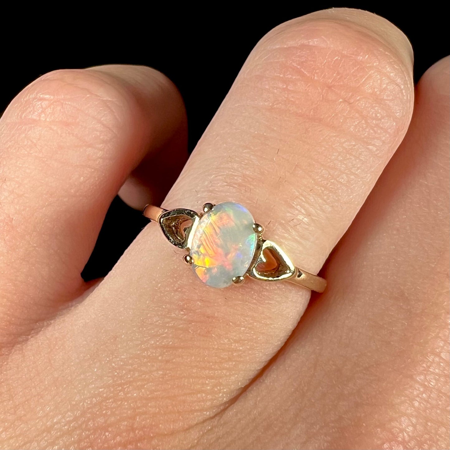 A dainty yellow gold ring mounted with a vivdly bright red Australian opal. The ring has two heart shaped designs.