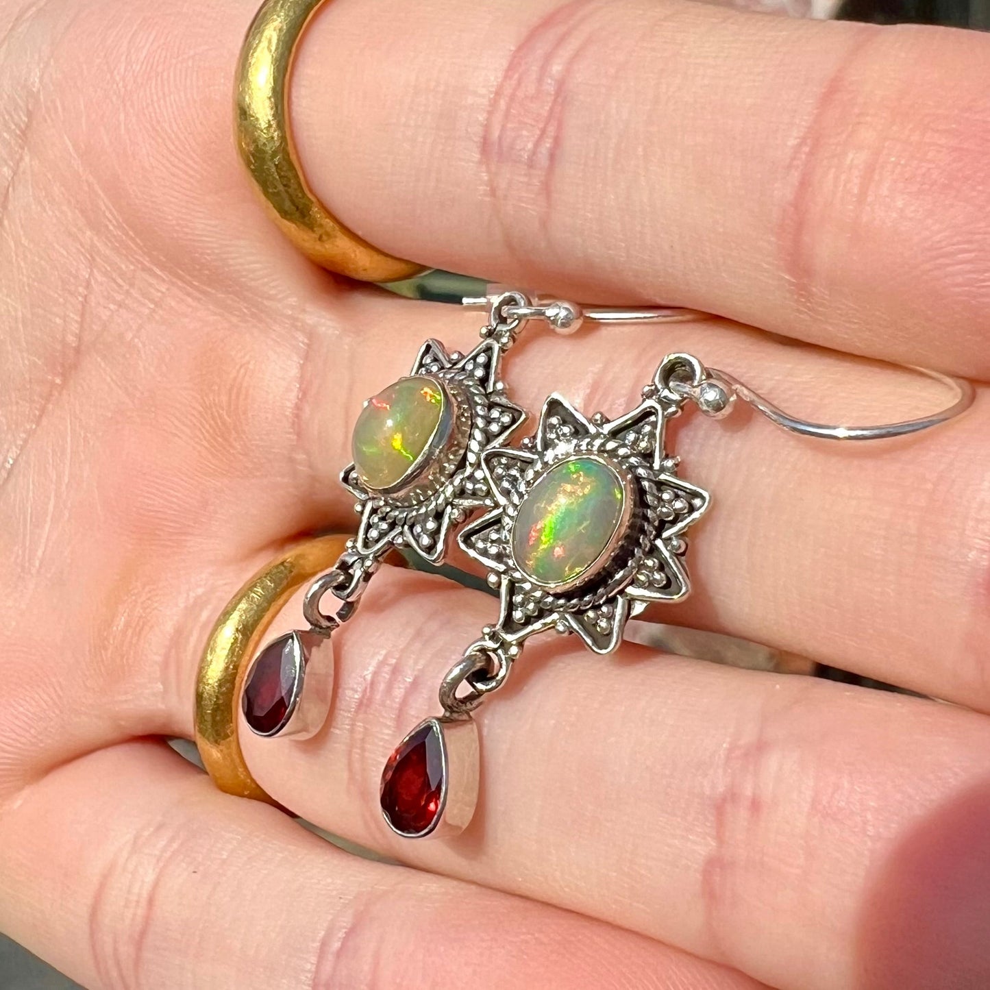 A pair of sterling silver star design dangle earrings set with Ethiopian fire opals and pear shaped red garnet accents.