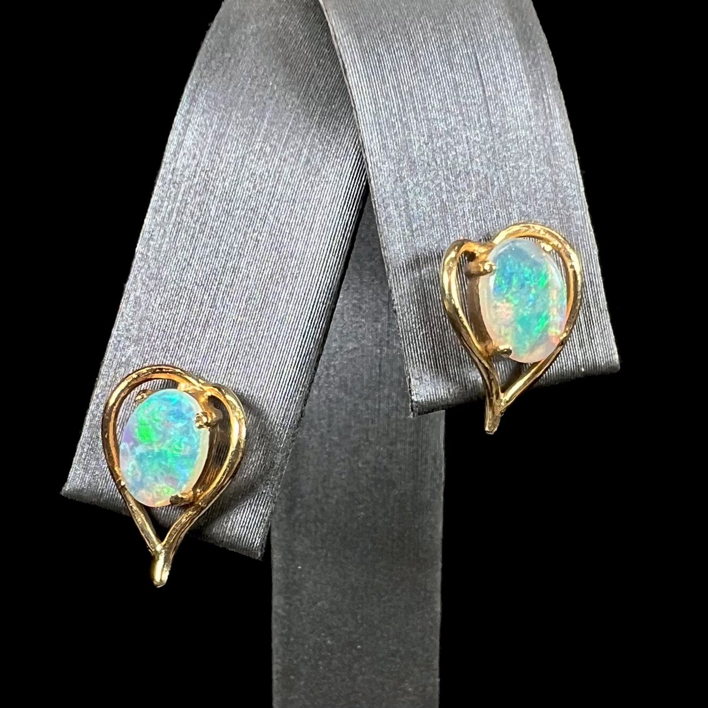 A pair of yellow gold, heart shaped stud earrings set with oval cabochon cut natural opal stones.