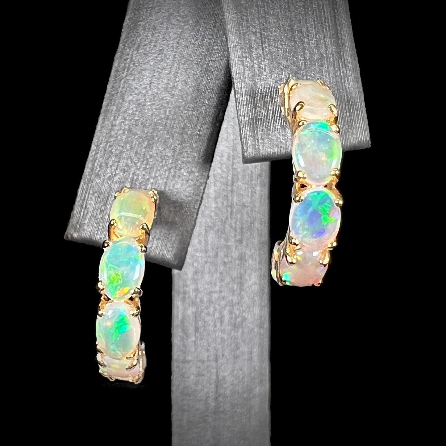A pair of yellow gold opal hoop earrings. Each earring is set with six natural oval cut opals.