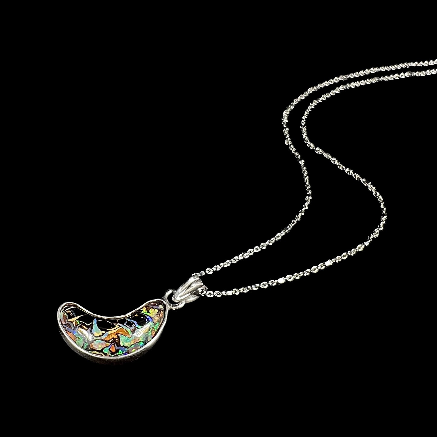 A sterling silver necklace bezel set with a natural Koroit boulder opal stone. The stone is shaped like a crescent moon.