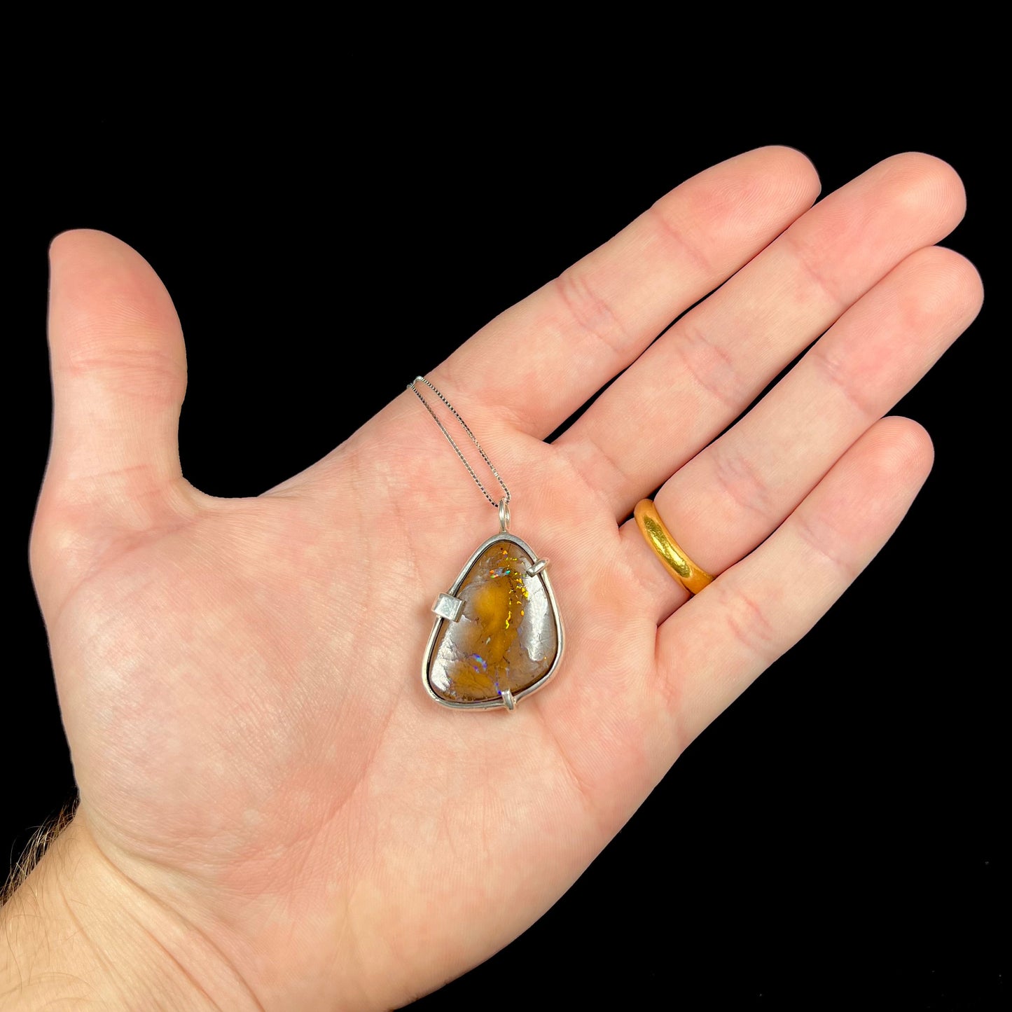 A handmade sterling silver pendant bezel and prong set with a natural boulder opal stone. The opal shines veins of color.