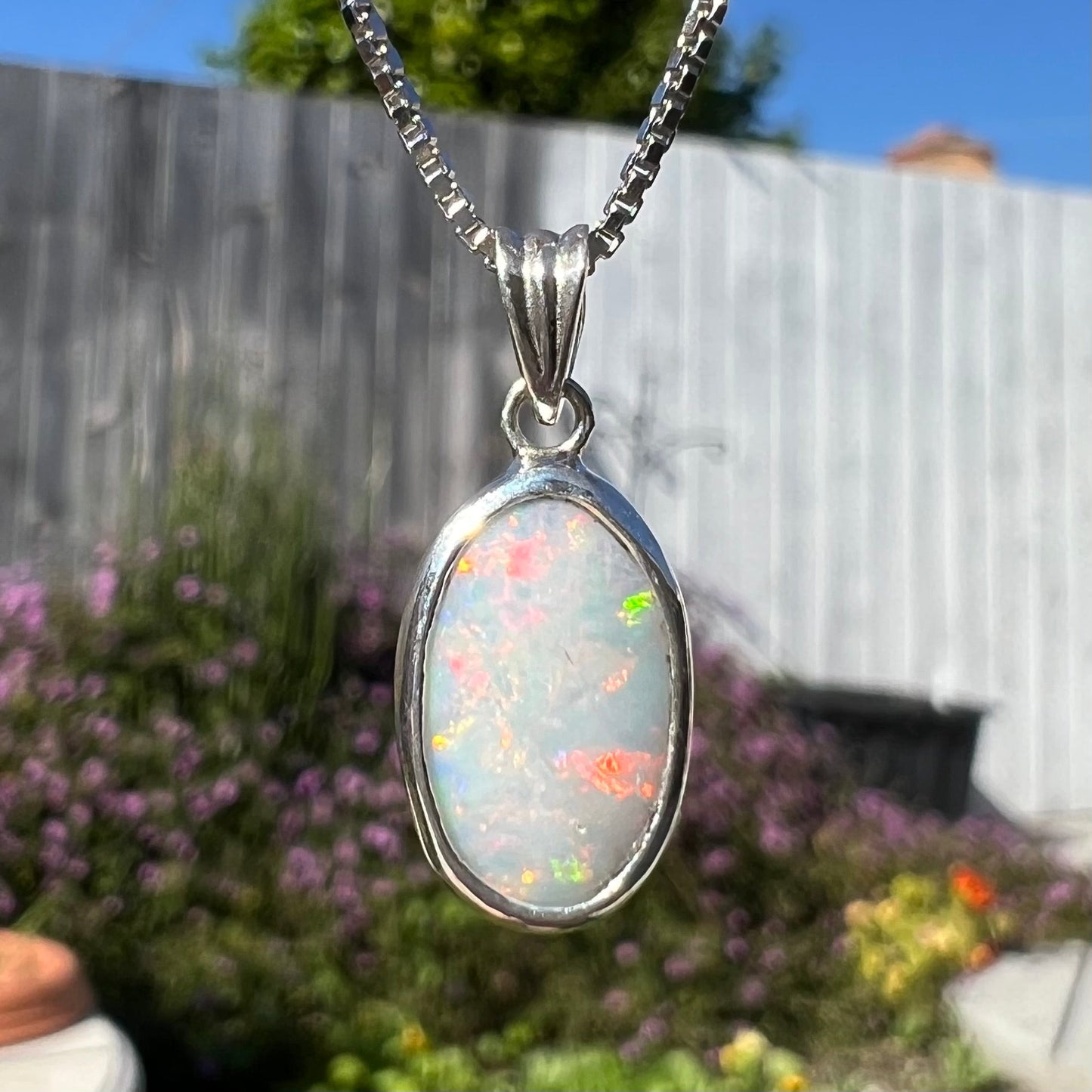 A ladies' sterling silver necklace bezel set with a natural white crystal opal. The opal has red and blue fire.