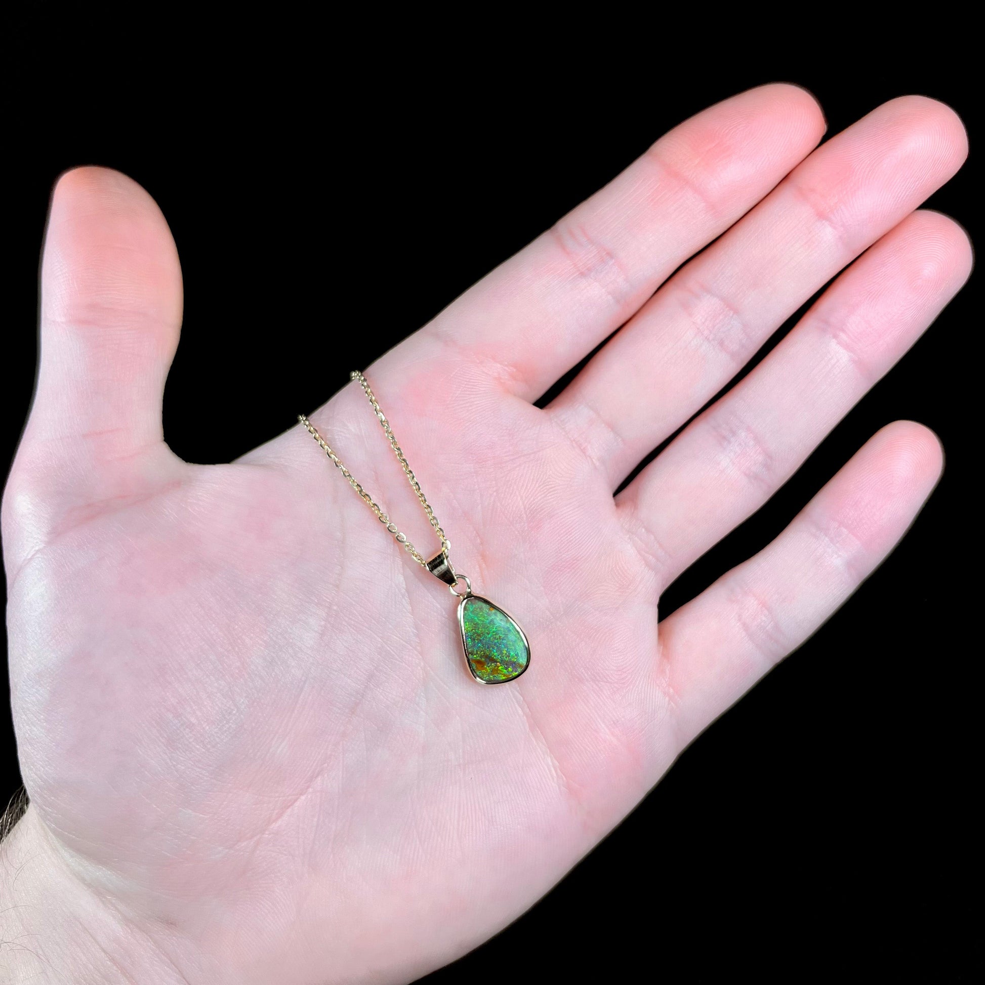A ladies' natural boulder opal necklace set in 14k yellow gold.  The opal is bezel set and shows green and blue colors.