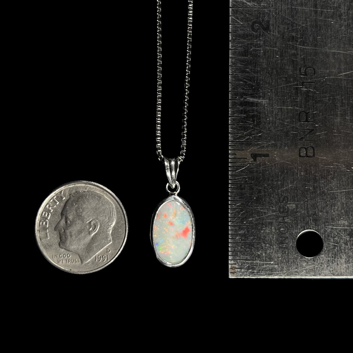 A ladies' sterling silver necklace bezel set with a natural white crystal opal. The opal has red and blue fire.