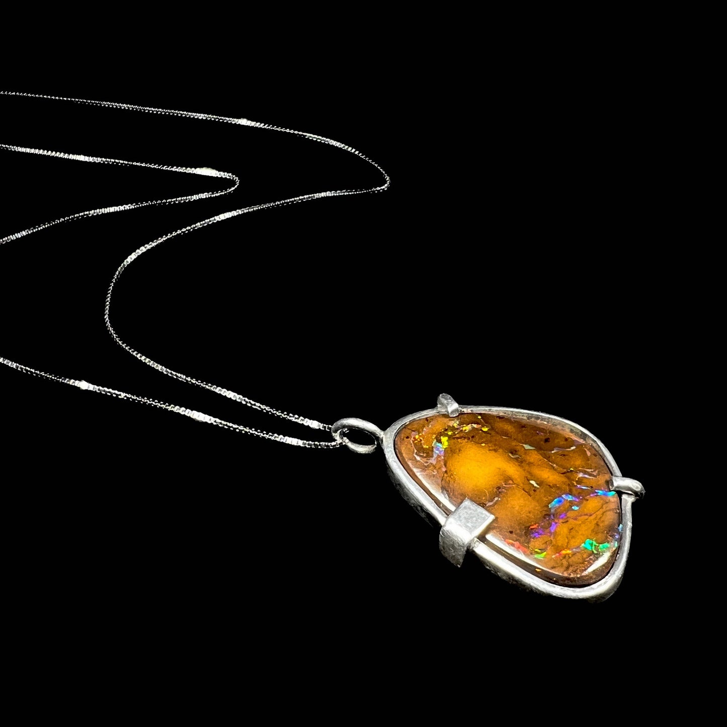 A handmade sterling silver pendant bezel and prong set with a natural boulder opal stone. The opal shines veins of color.