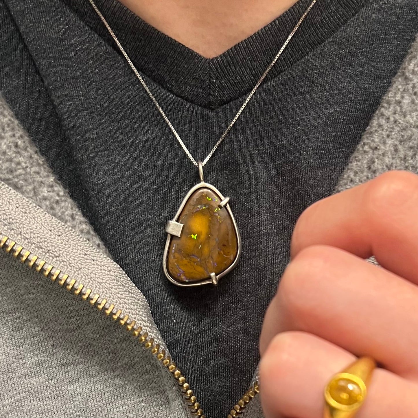 A handmade sterling silver pendant bezel and prong set with a natural boulder opal stone. The opal shines veins of color.