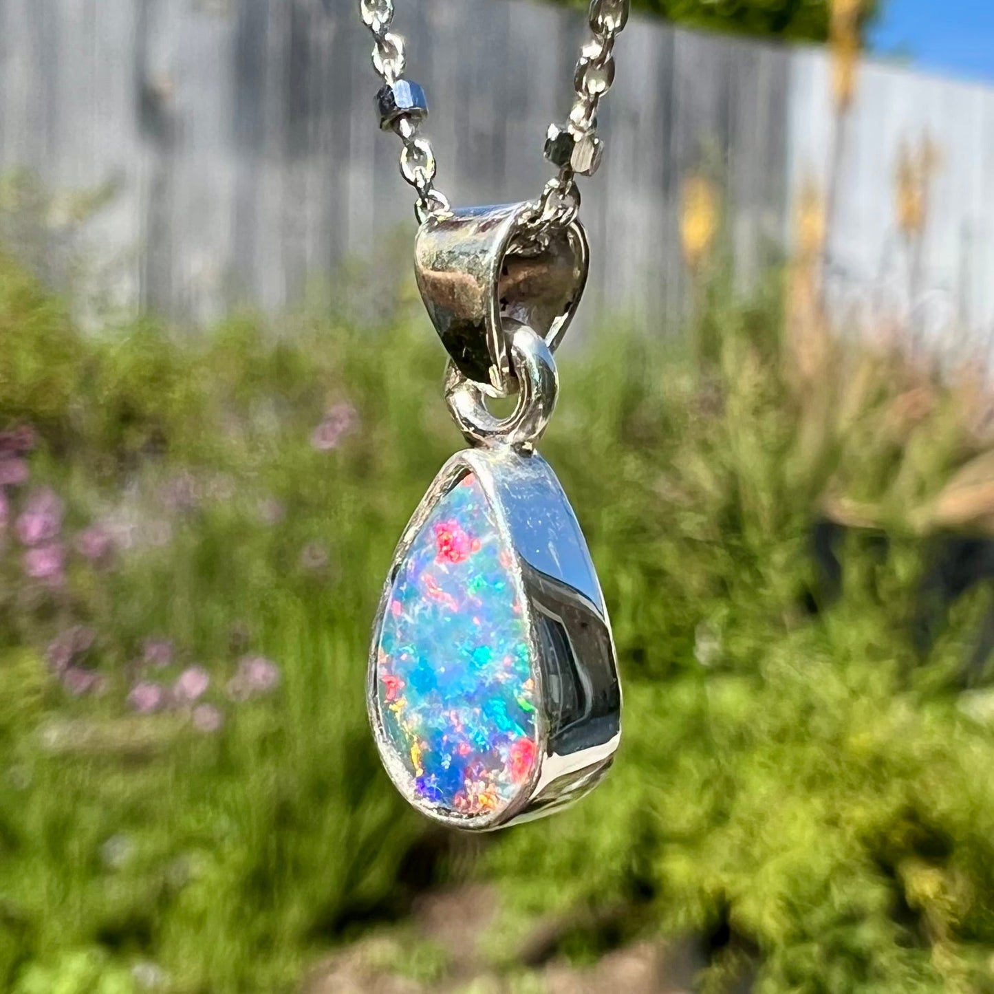 A pear shaped black opal necklace set in sterling silver. The opal vividly flashes every color of the rainbow.