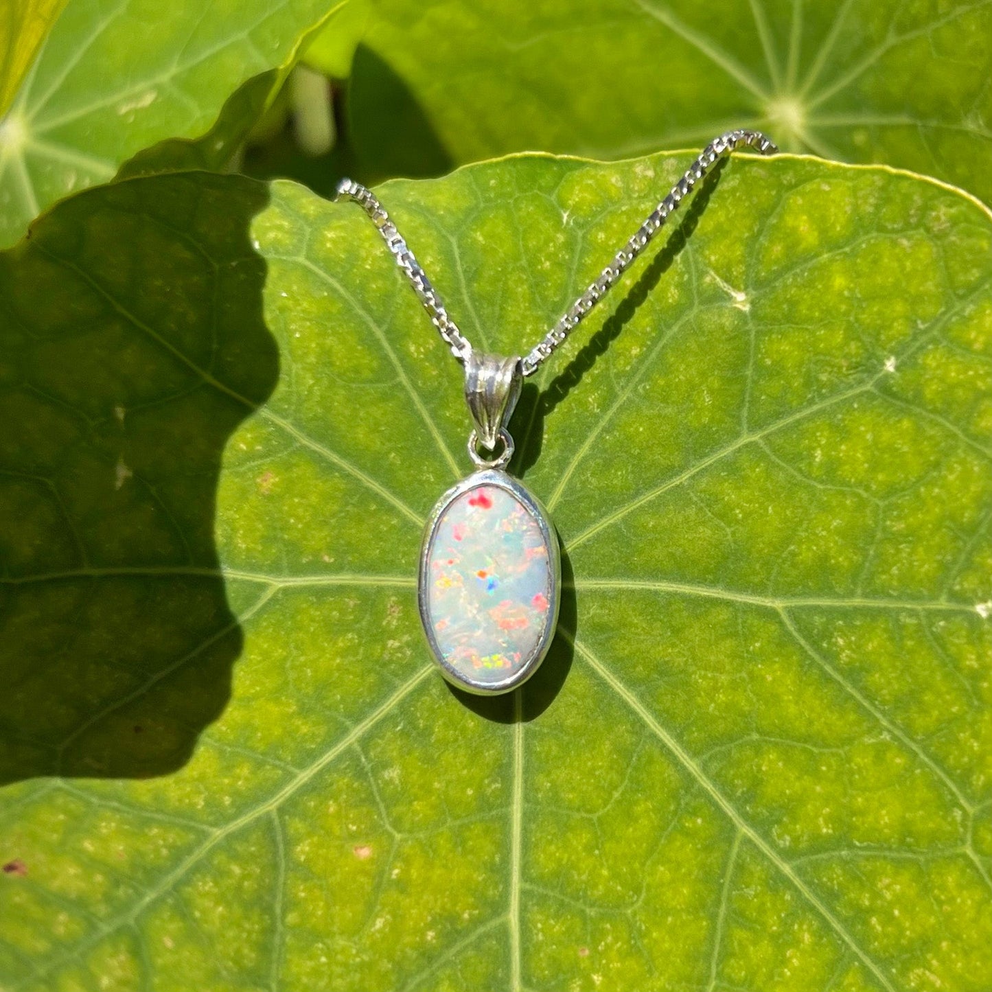 A ladies' sterling silver necklace bezel set with a natural white crystal opal. The opal has red and blue fire.