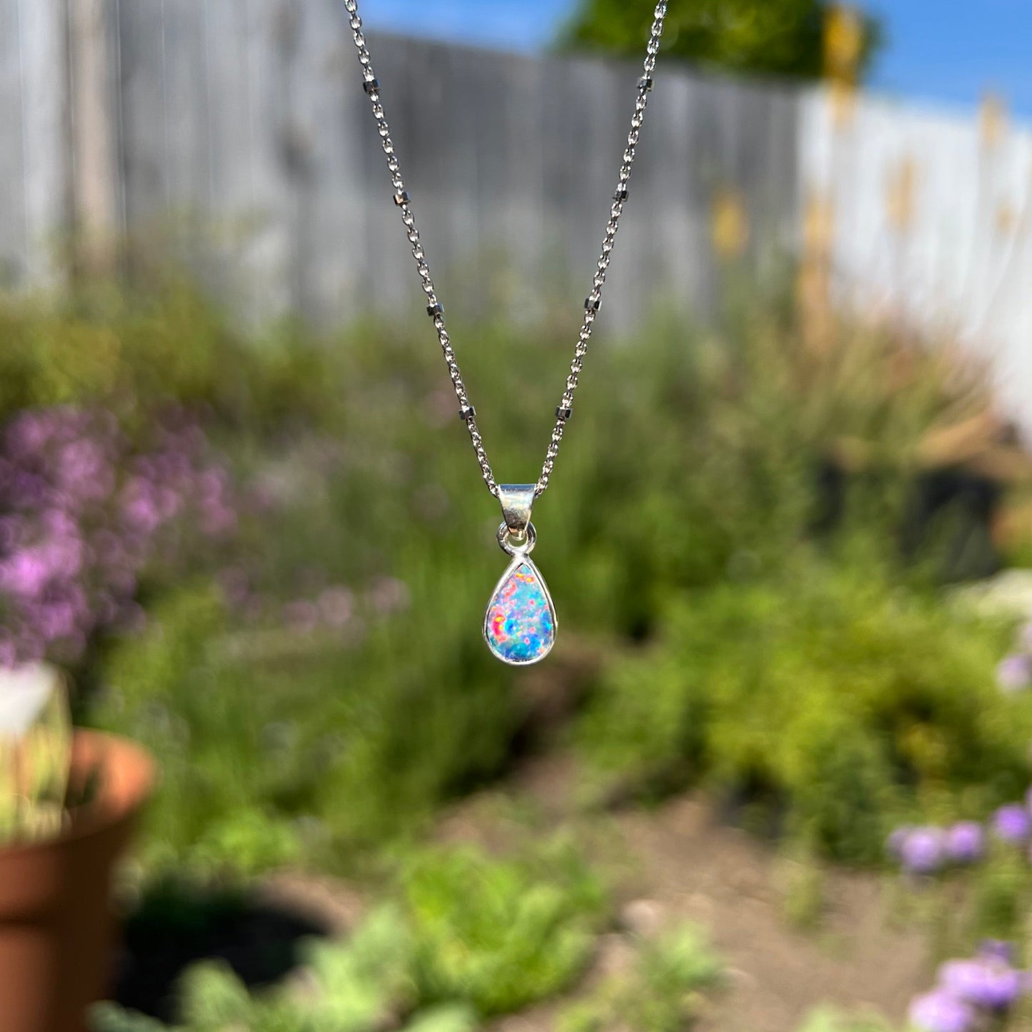 A pear shaped black opal necklace set in sterling silver. The opal vividly flashes every color of the rainbow.