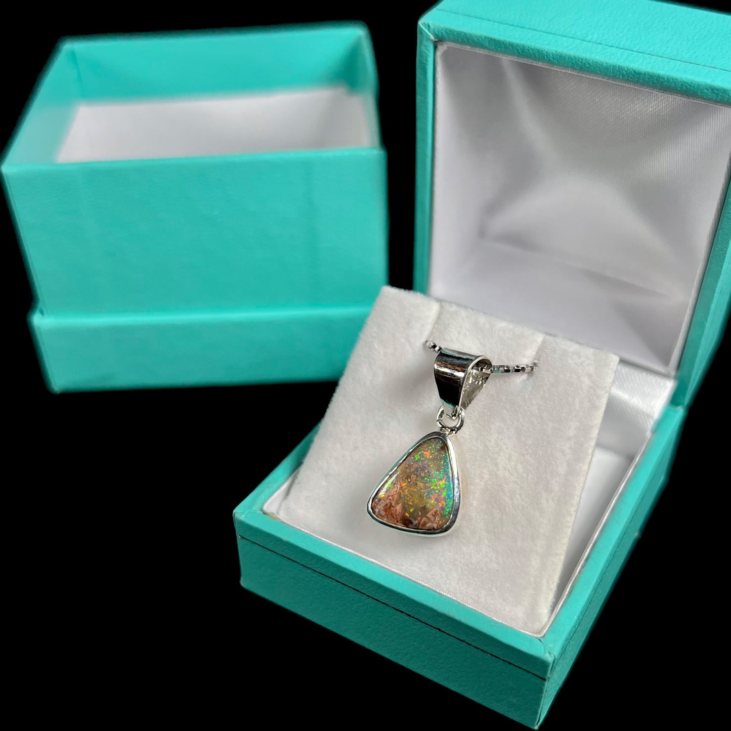 A sterling silver boulder opal necklace on a box chain. The opal twinkles bright red, green, and blue colors.
