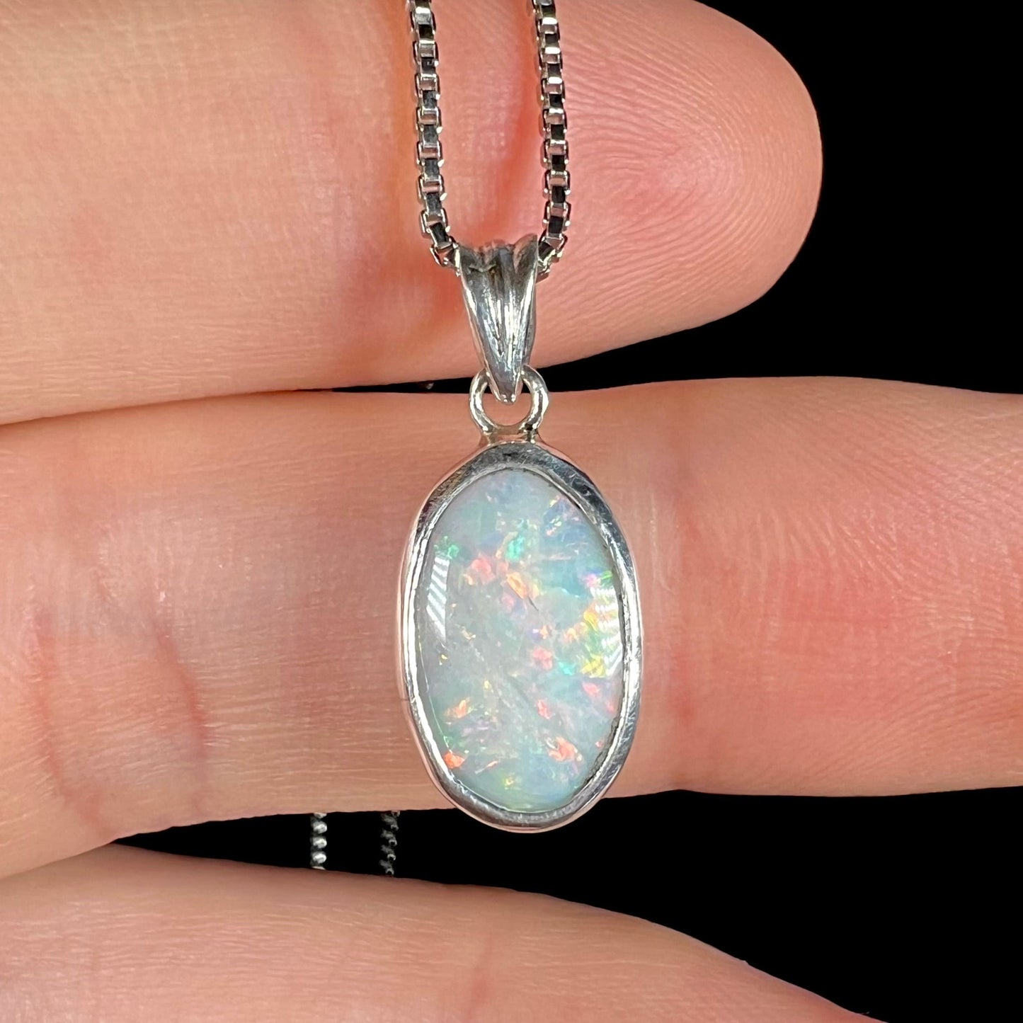 A ladies' sterling silver necklace bezel set with a natural white crystal opal. The opal has red and blue fire.