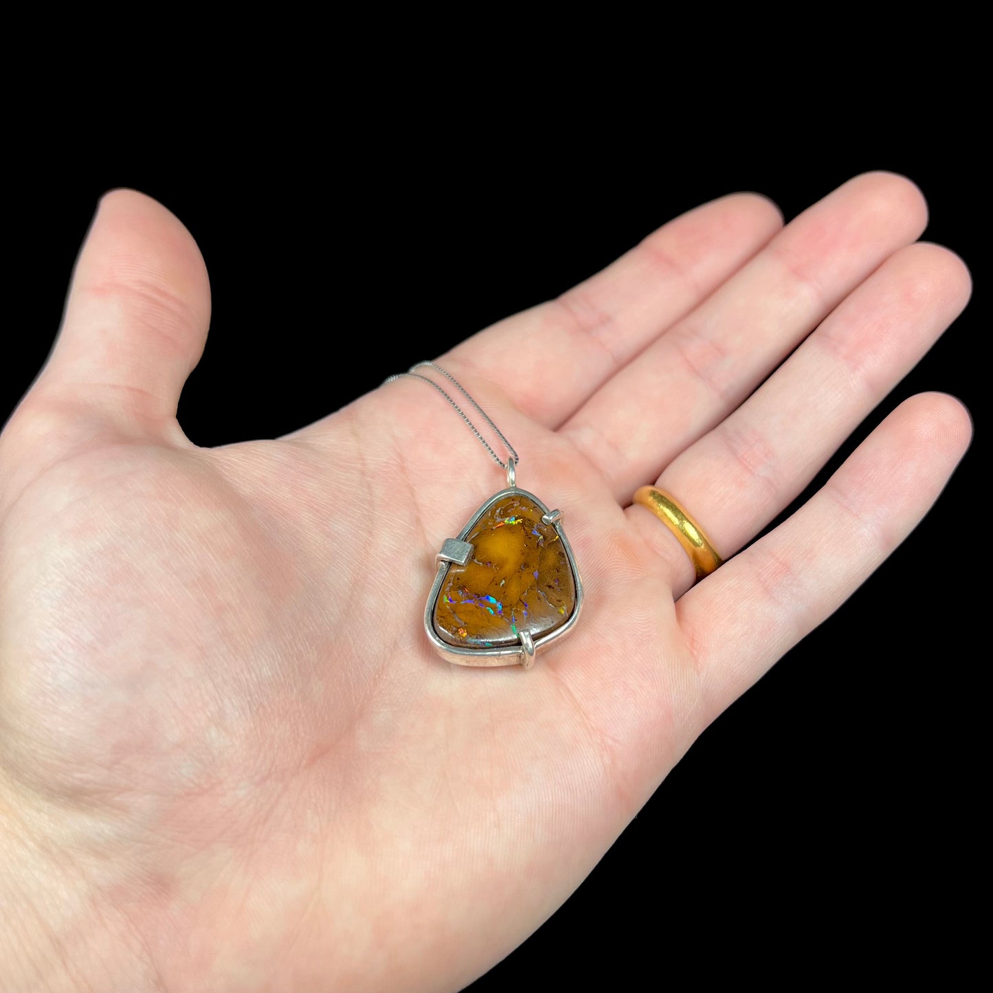 A handmade sterling silver pendant bezel and prong set with a natural boulder opal stone. The opal shines veins of color.