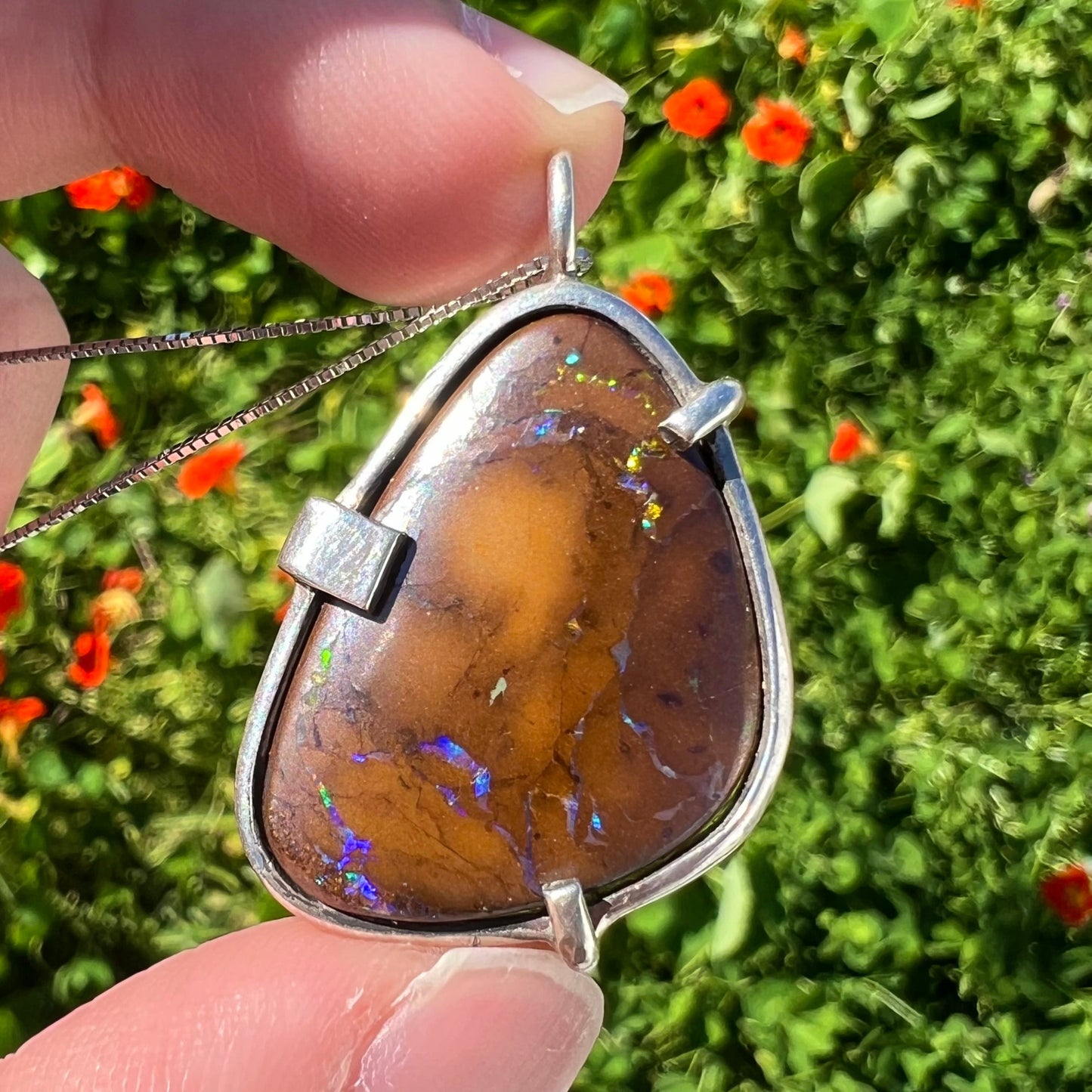 A handmade sterling silver pendant bezel and prong set with a natural boulder opal stone. The opal shines veins of color.