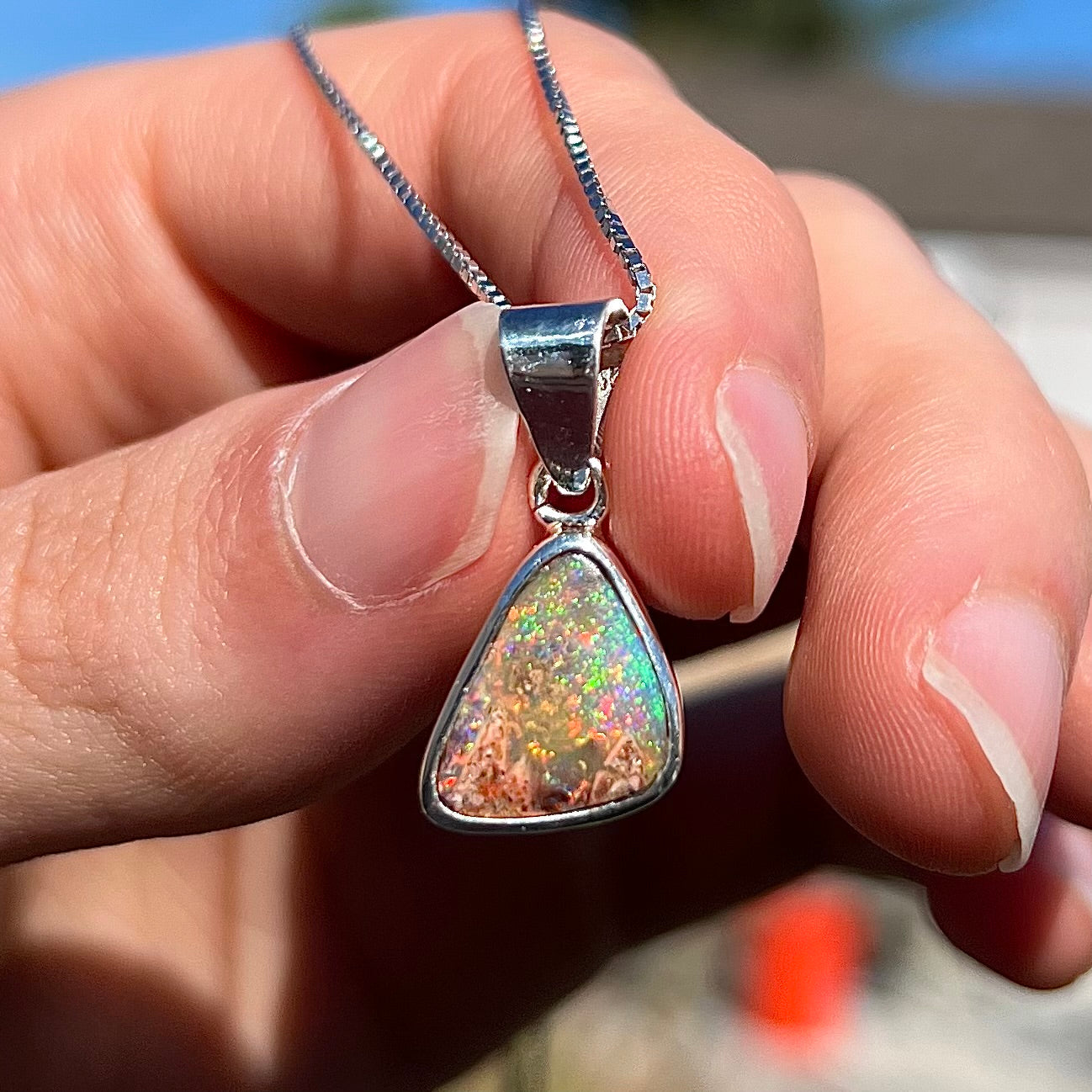 A sterling silver boulder opal necklace on a box chain. The opal twinkles bright red, green, and blue colors.