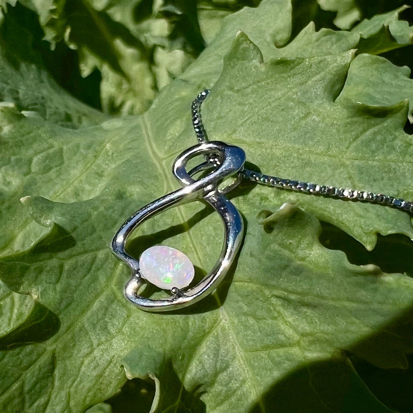 A ladies' sterling silver necklace set with an oval cabochon cut natural white crystal opal with green fire.