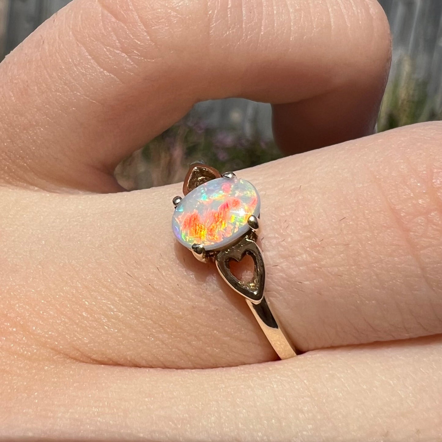 A dainty yellow gold ring mounted with a vivdly bright red Australian opal. The ring has two heart shaped designs.
