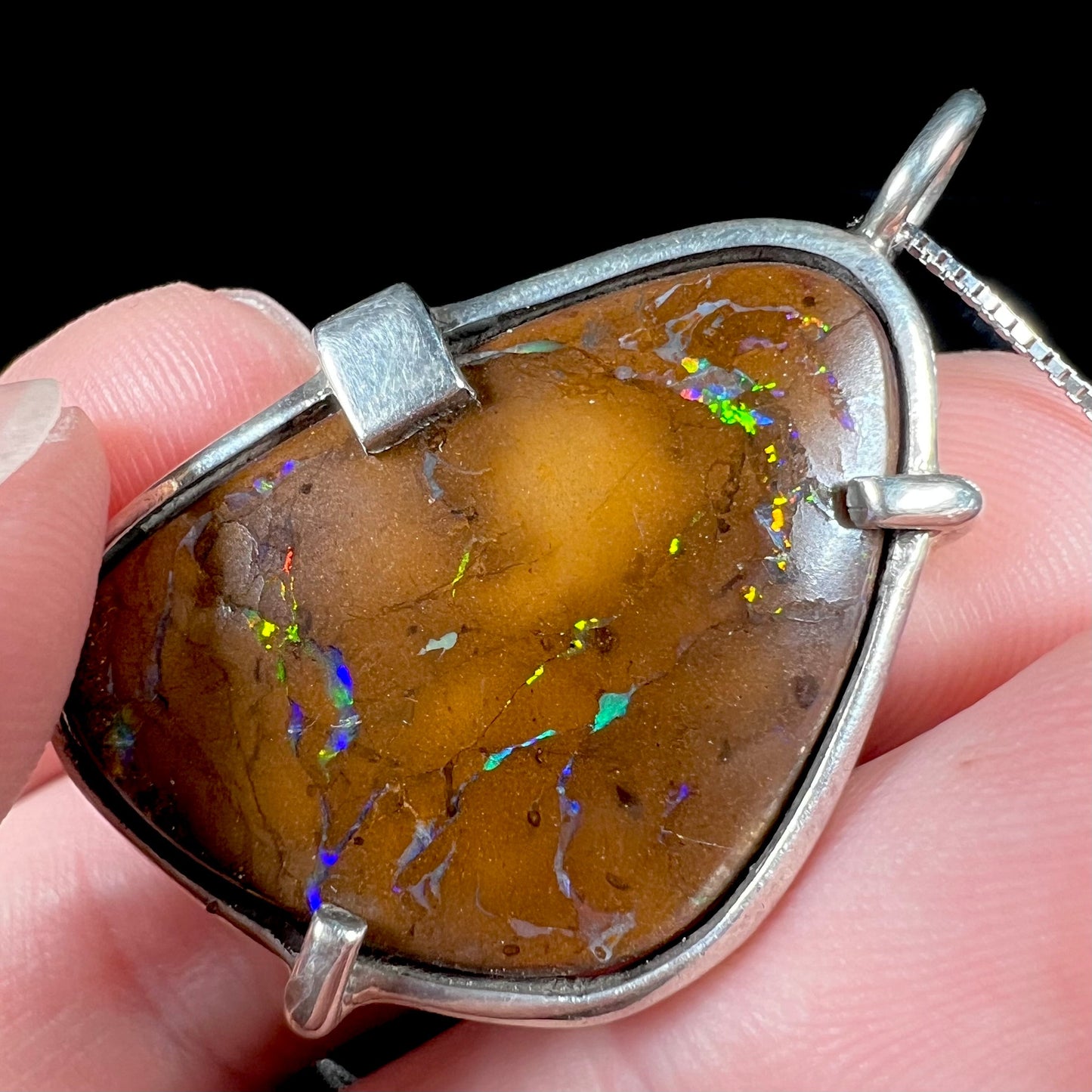 A handmade sterling silver pendant bezel and prong set with a natural boulder opal stone. The opal shines veins of color.