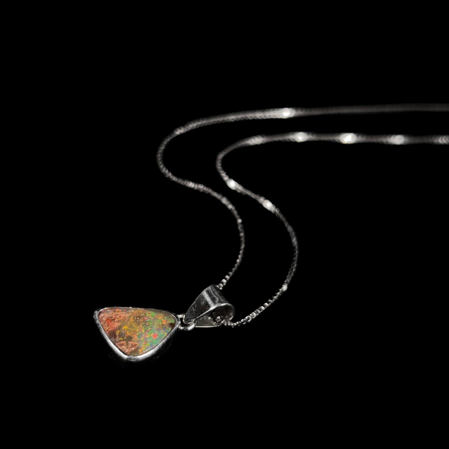 A sterling silver boulder opal necklace on a box chain. The opal twinkles bright red, green, and blue colors.