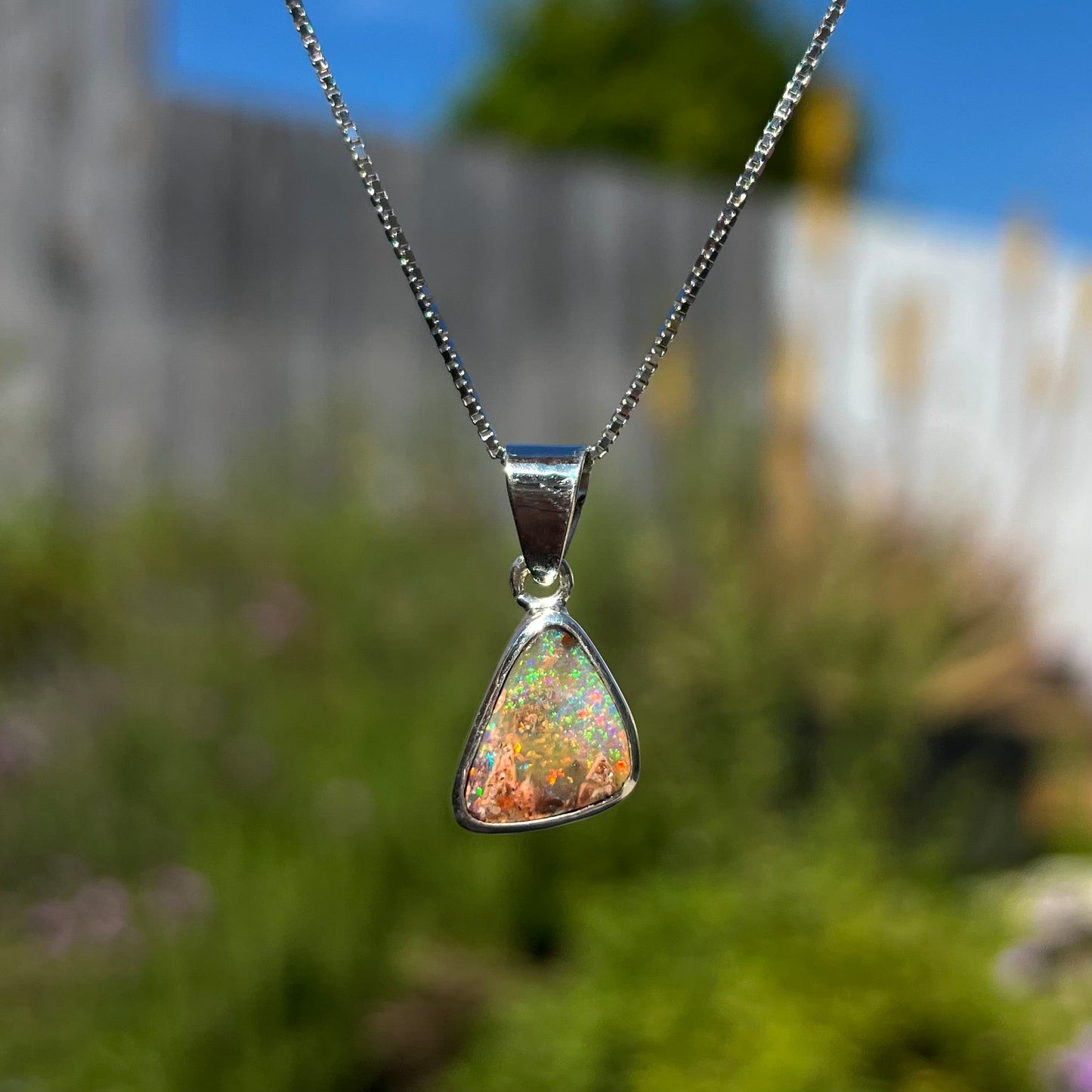 A sterling silver boulder opal necklace on a box chain. The opal twinkles bright red, green, and blue colors.