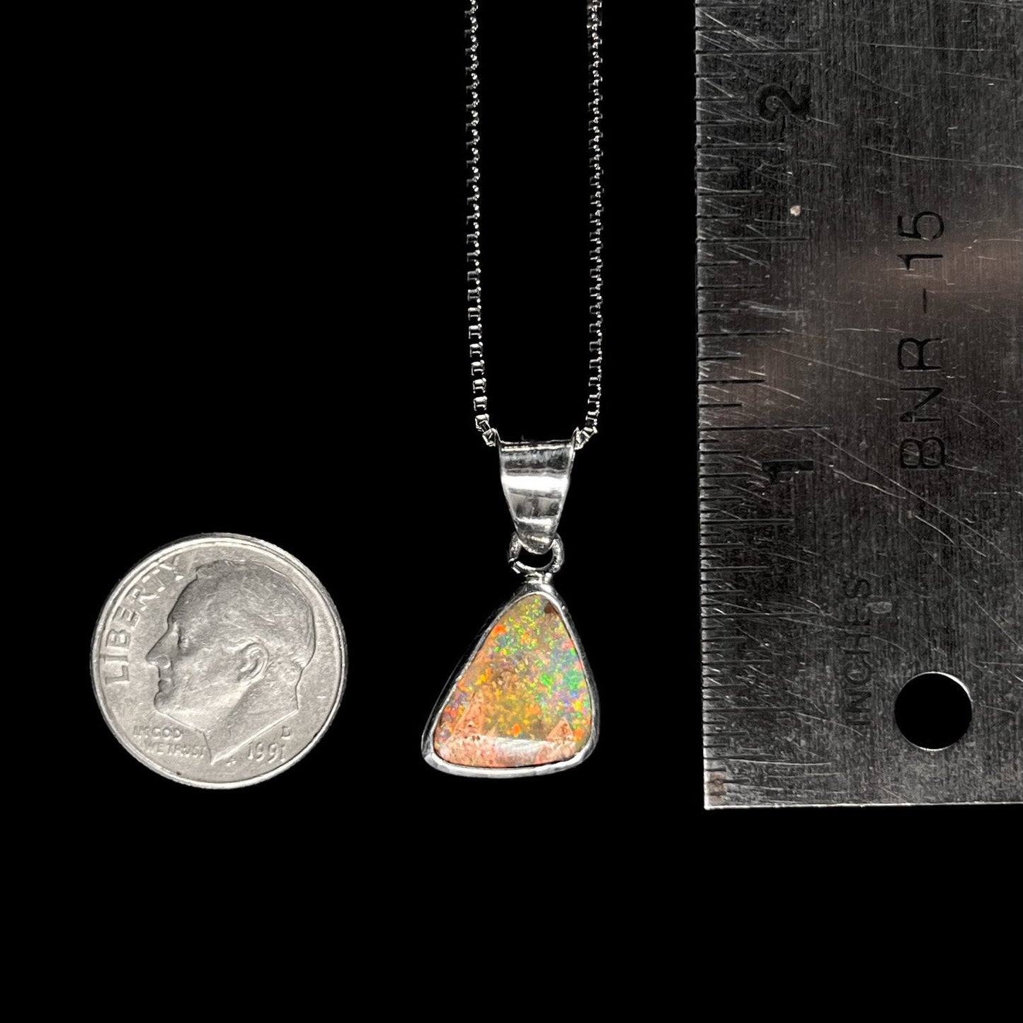 A sterling silver boulder opal necklace on a box chain. The opal twinkles bright red, green, and blue colors.