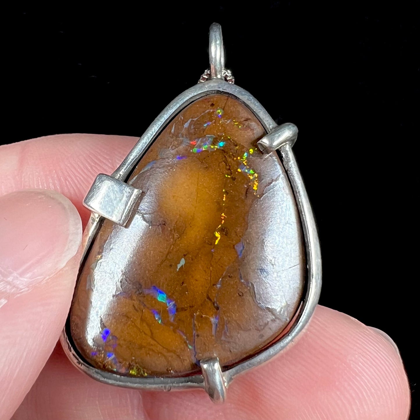 A handmade sterling silver pendant bezel and prong set with a natural boulder opal stone. The opal shines veins of color.